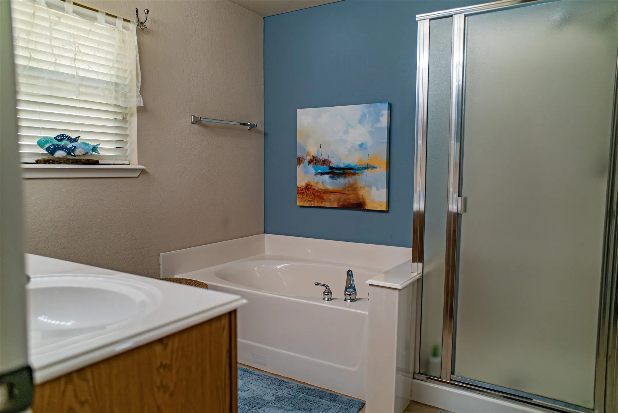 Bathroom featuring a built-in soaking tub with deck-mounted fixtures, a separate shower enclosure with frosted glass, a vanity with an integrated sink, and a window with blinds