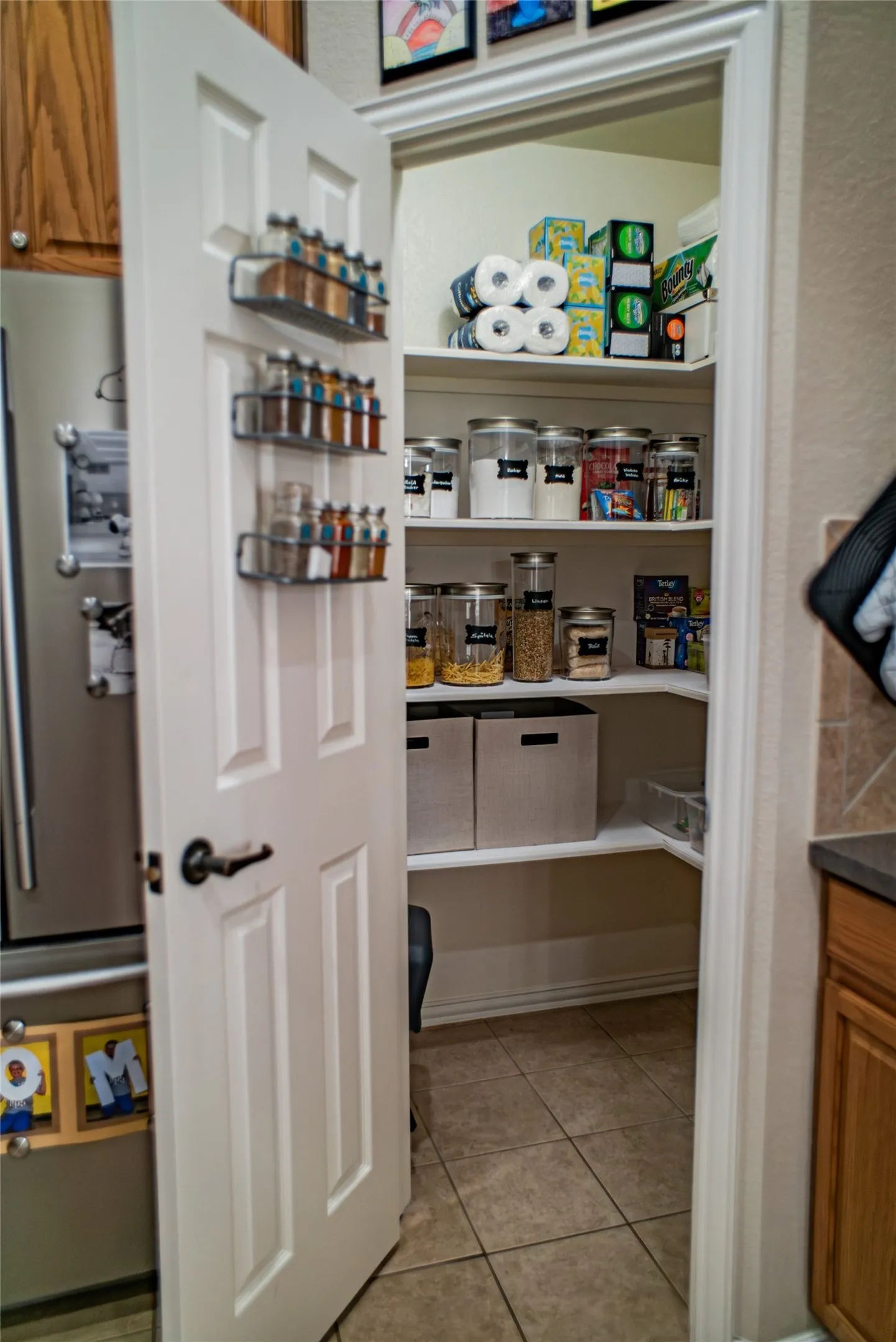 Pantry featuring L-shaped shelving, tile flooring, and a six-panel door with matte black hardware