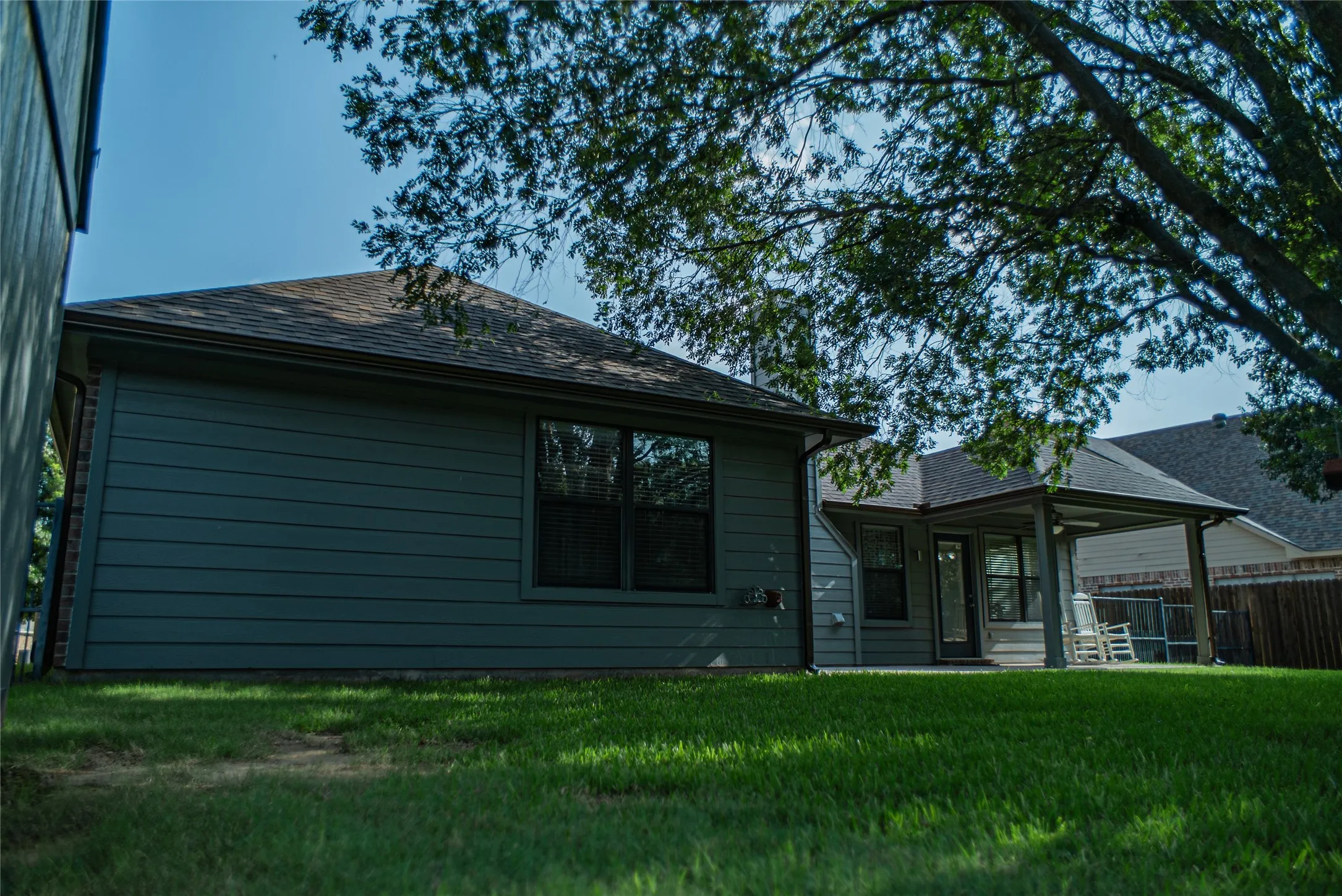 Expansive green lawn featuring a covered patio, dark siding, and a fenced perimeter