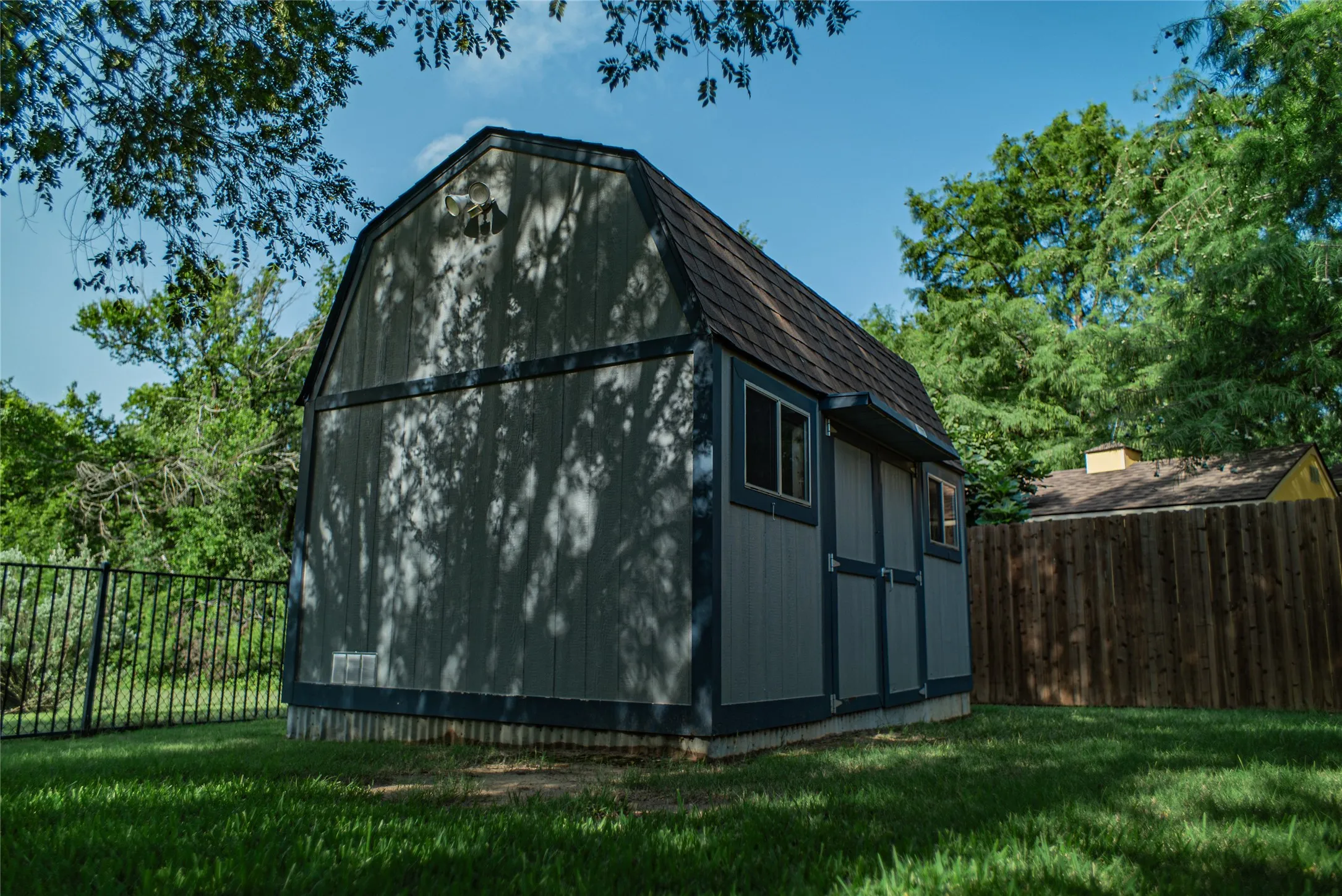 Gambrel-roofed storage shed with siding exterior and multiple windows