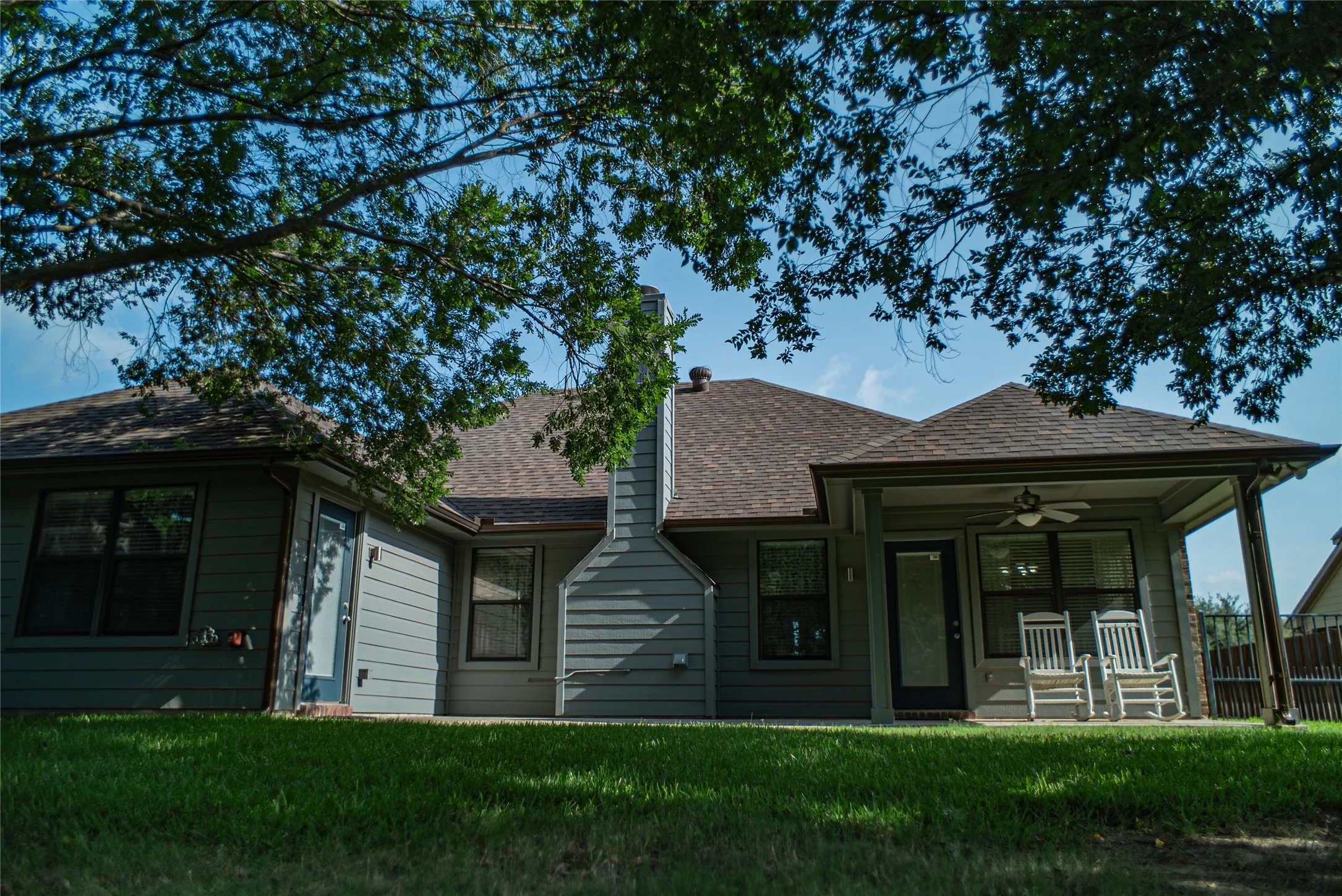 Rear exterior featuring a covered patio with an outdoor ceiling fan, multiple windows, a backdoor entry, and a​​‌​​​​‌​​‌‌​‌‌​​​‌‌​‌​‌​‌​​​‌​​ chimney