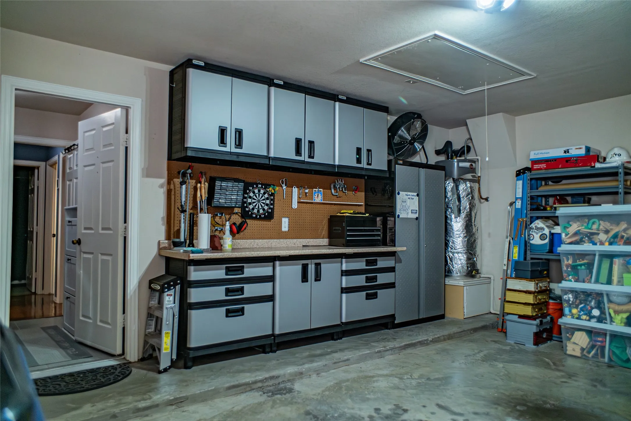 Garage workspace featuring a built-in countertop, pegboard organization, and overhead cabinetry