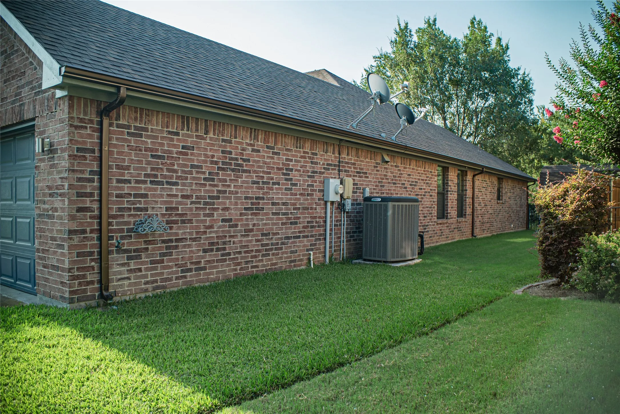 Brick exterior with a dark-shingle roof, featuring a gray panel garage door and a green lawn