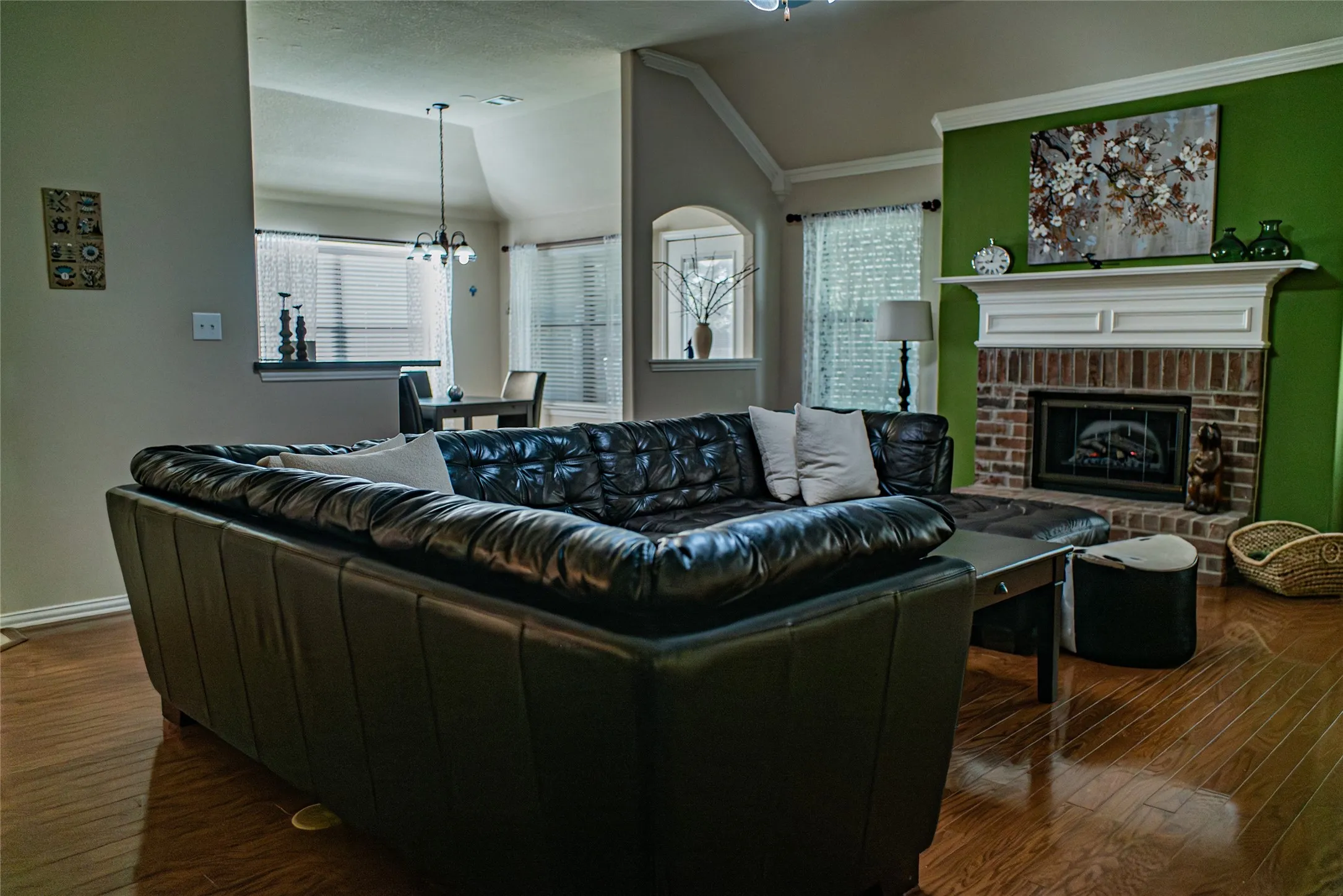Living area featuring wood-finish flooring, a brick fireplace with a white mantel, vaulted ceilings, and an open pass-through to a dining space