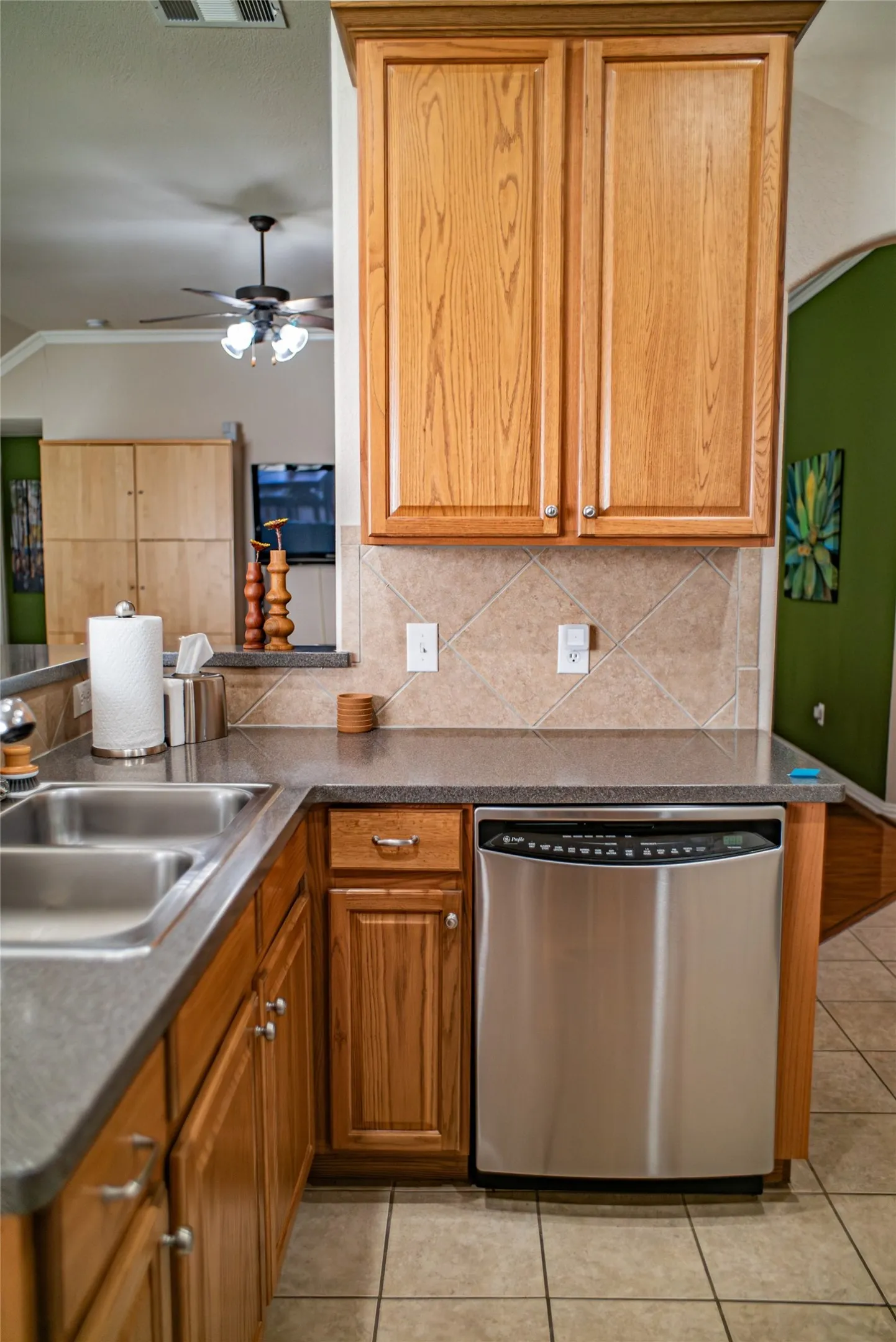 Kitchen featuring light wood cabinetry, a stainless steel dishwasher, a double basin sink, and tile flooring