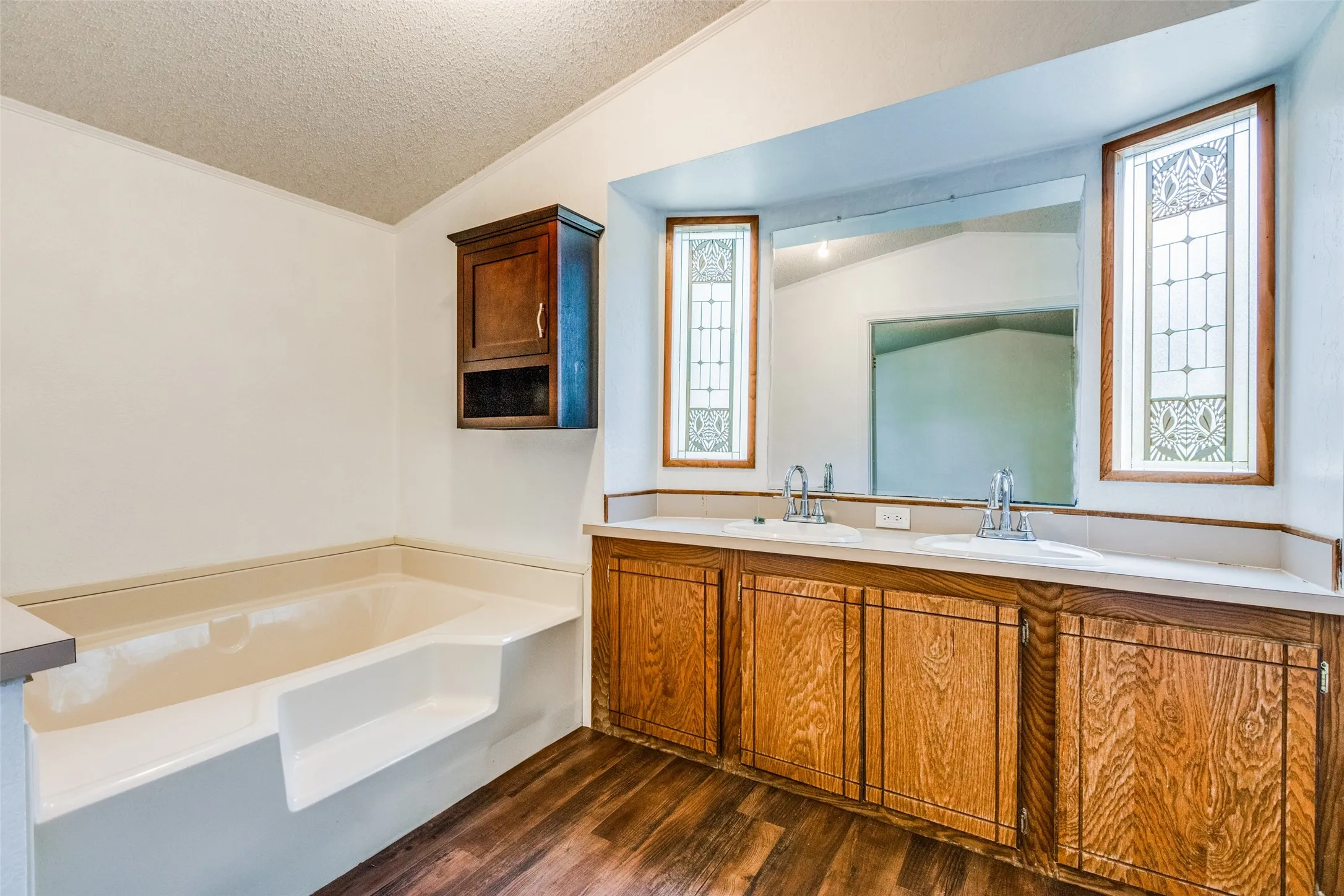 Ensuite Bathroom featuring vaulted ceiling, hardwood/ wood-style floors, plenty of natural light, double sinks with large vanity and a large soaking tub.