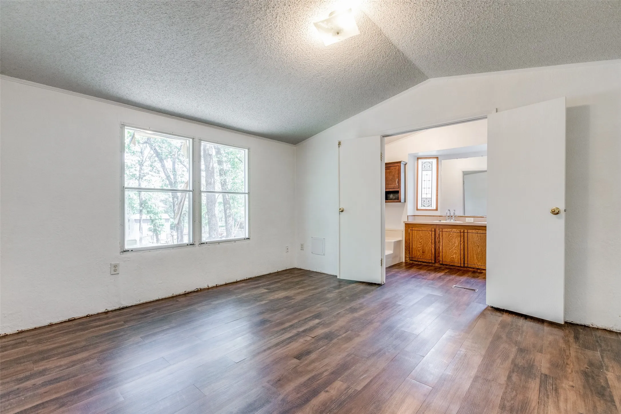 Primary bedroom featuring dark hardwood/wood-style floors, ensuite bathroom, vaulted ceiling, and a textured ceiling.