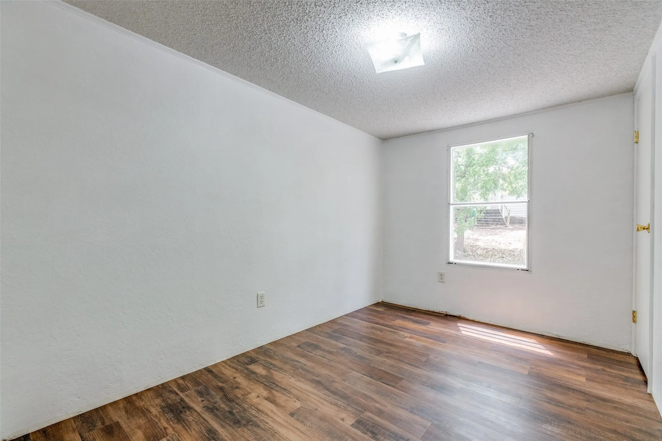 Smaller secondary bedroom with dark hardwood/wood-style flooring and a textured ceiling.