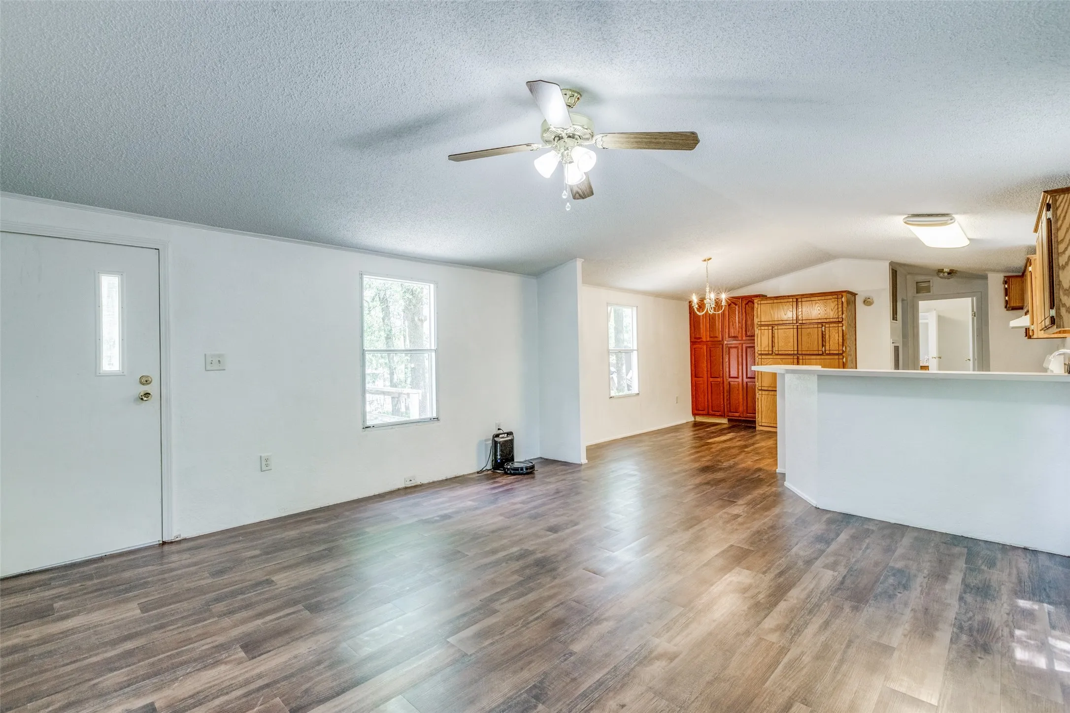 Unfurnished family room, lofted ceiling with ceiling fan overlooking dining room with notable chandelier, built in cabinets for storage and dark hardwood/wood-style floors.