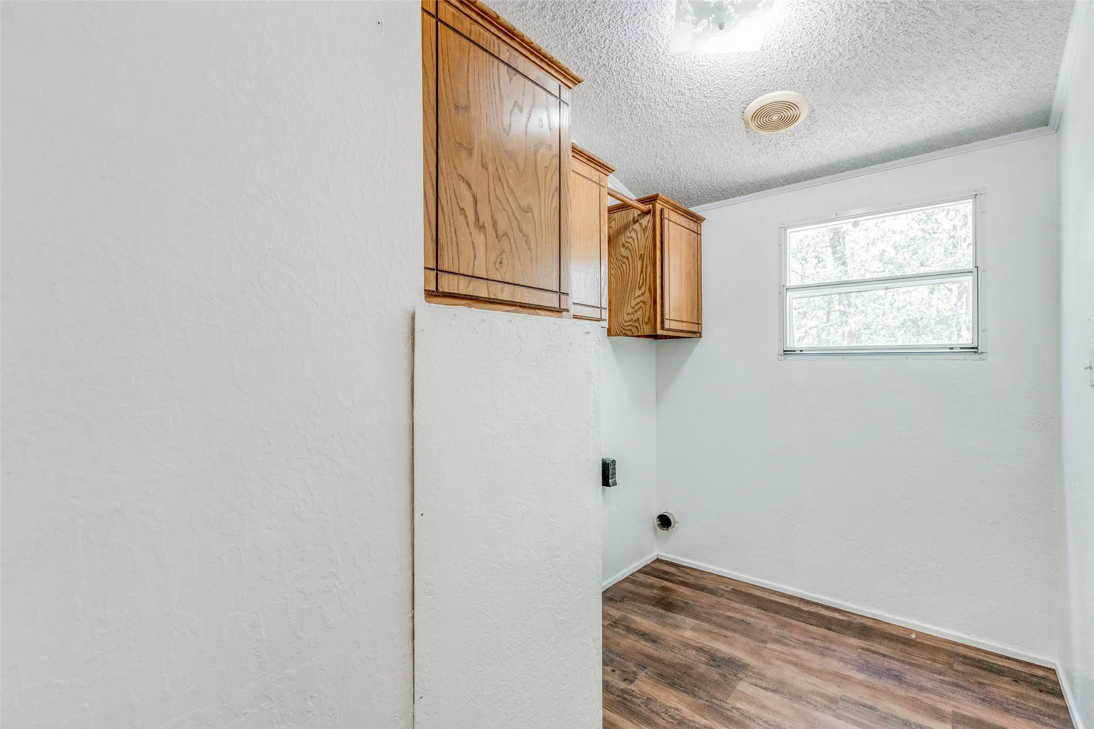 Laundry area featuring cabinets above washer and dryer area and hanging rod, dark hardwood/ wood-style floors, and a textured ceiling.