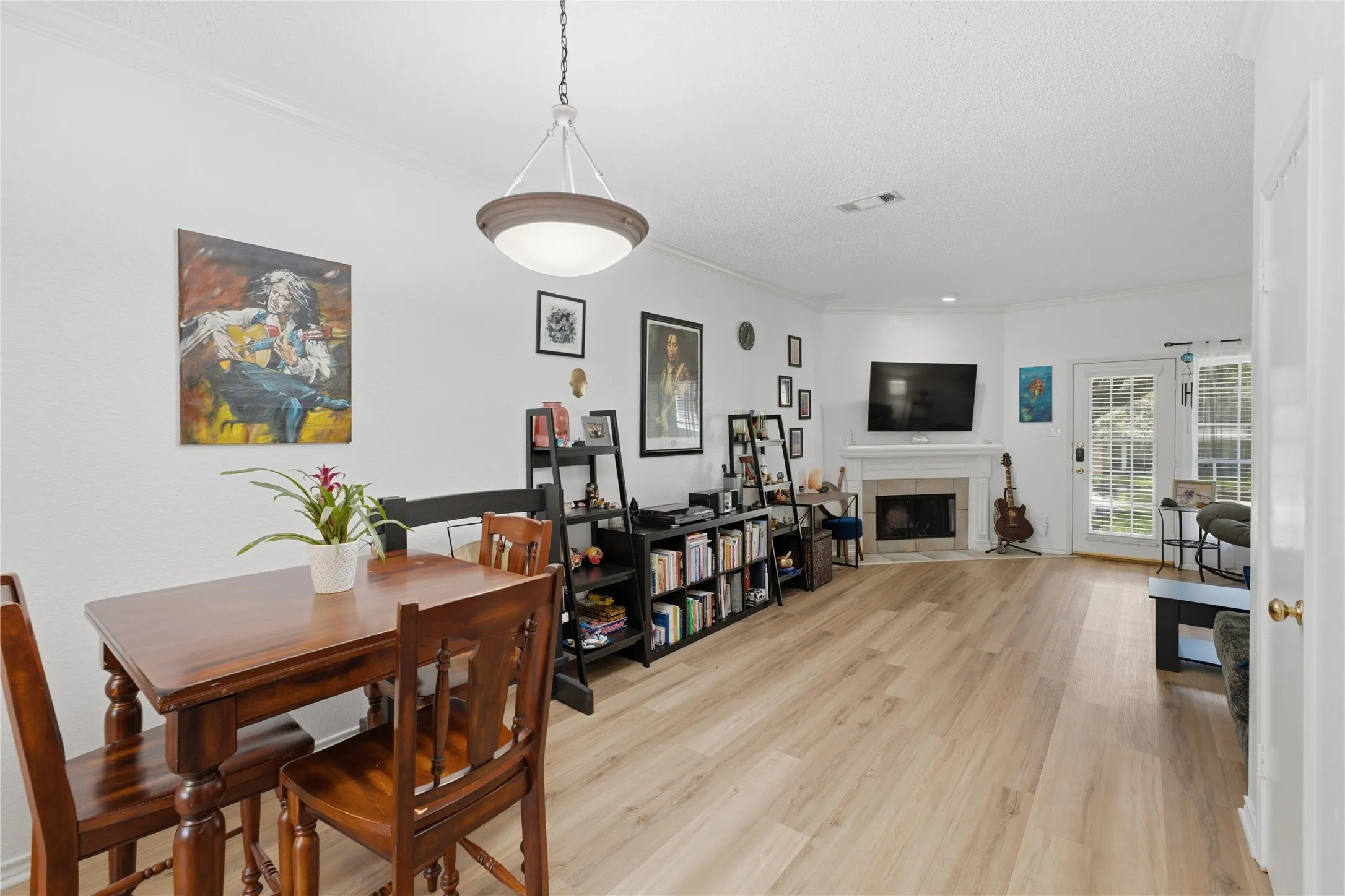 Open-concept living area with wood-finish flooring, a corner fireplace featuring a white mantel, and ceiling crown molding