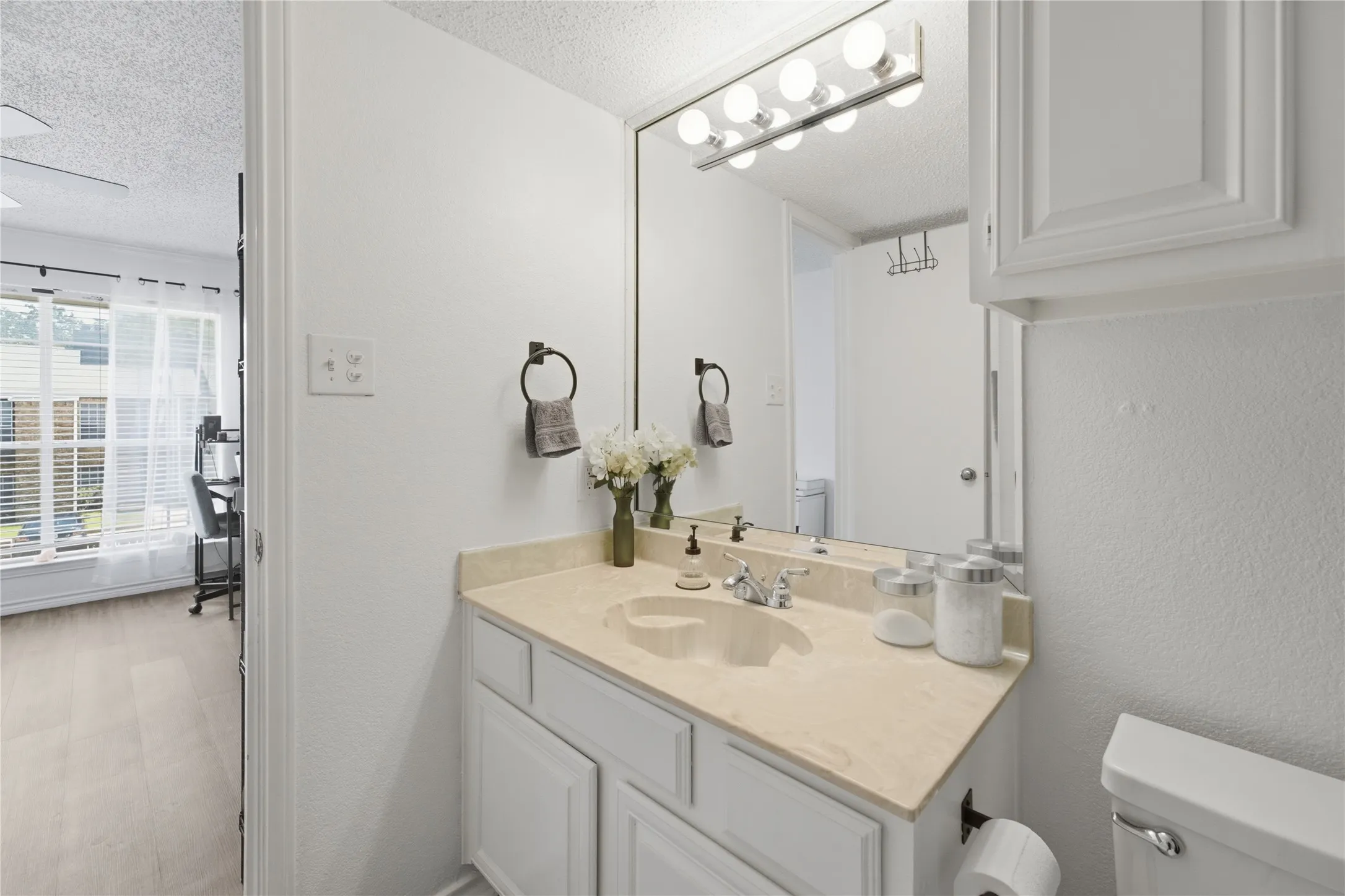 Bathroom featuring a single vanity with a light-toned countertop, white cabinetry, a built-in mirror, and overhead strip lighting