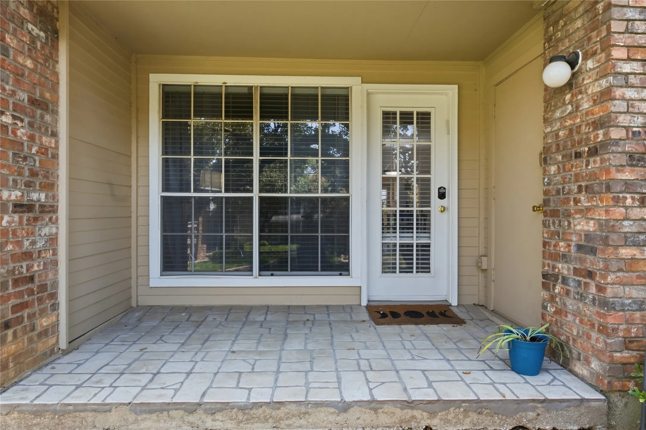 Covered patio entrance featuring a French door with multiple glass panes, a large window with gridded panes, brick exterior, and neutral-toned siding