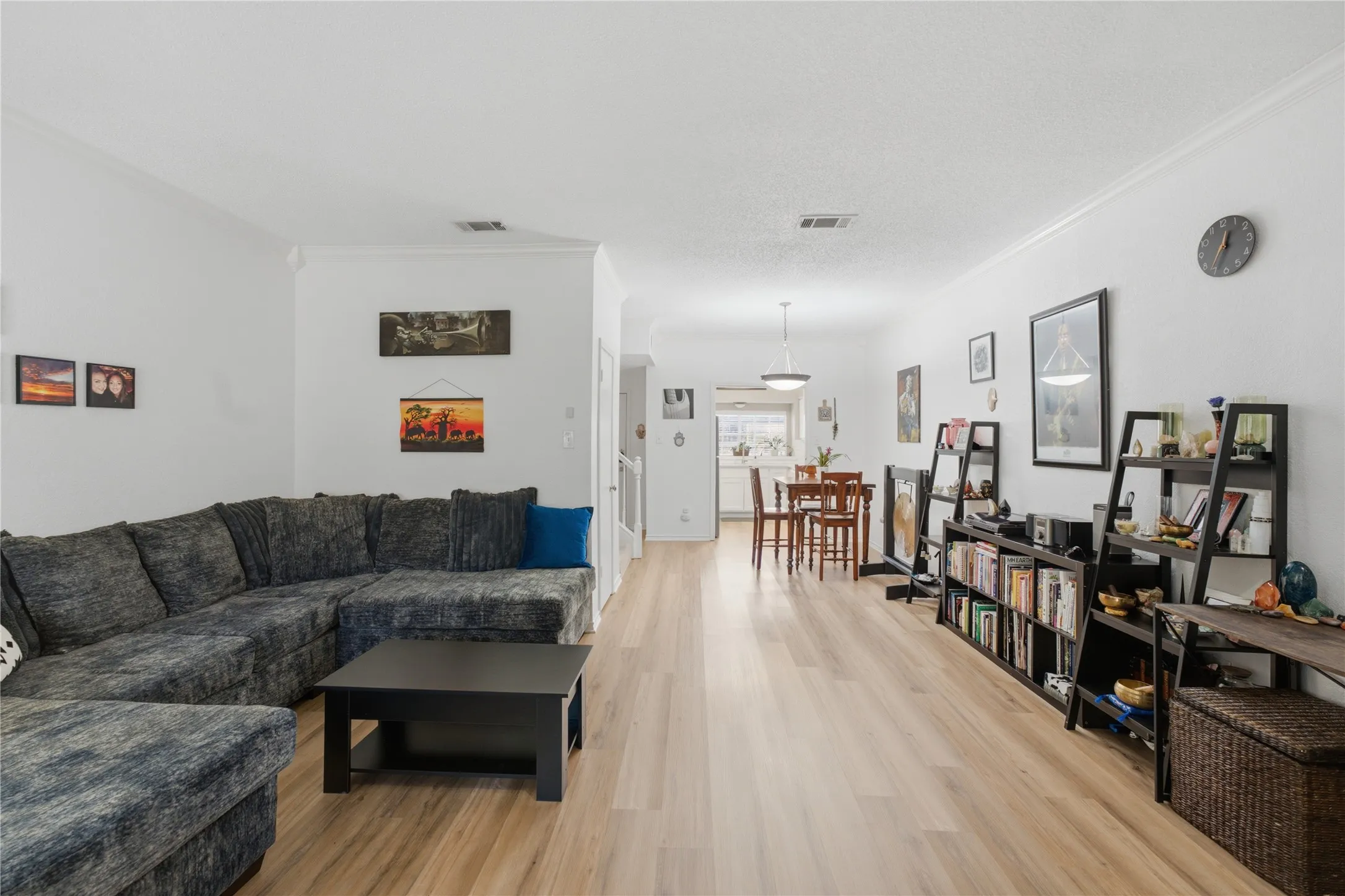 Open-concept living space featuring light wood-finish flooring, white walls, and crown molding
