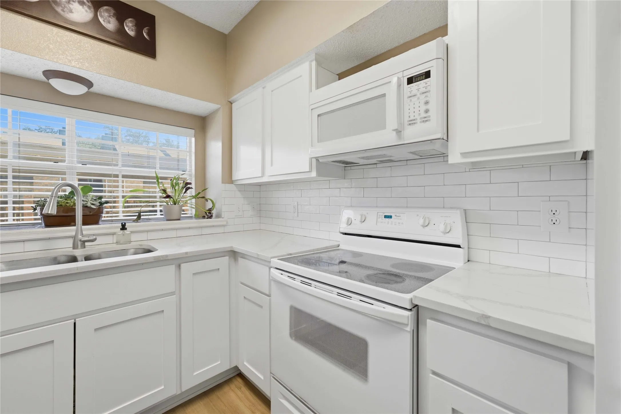 Kitchen featuring white shaker-style cabinetry, a stainless steel double basin sink with a high-arc faucet, and white subway tile backsplash