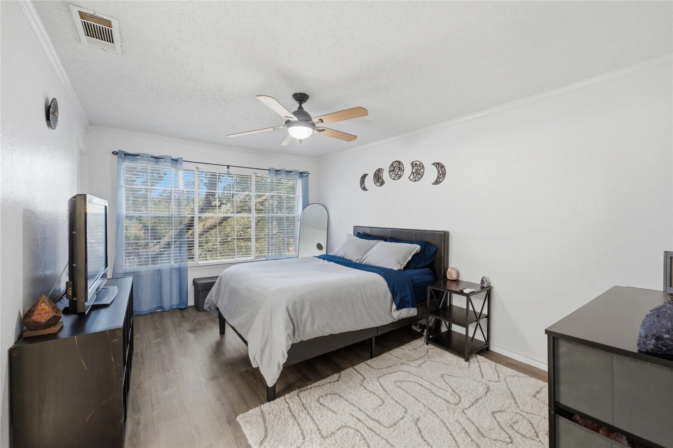 Spacious room featuring wood-finish flooring, a window with horizontal blinds, a ceiling fan with integrated lighting, and crown molding