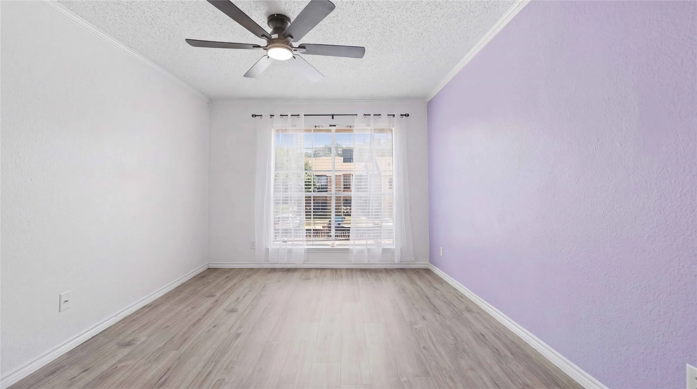 Wood-finish flooring, ceiling fan with integrated lighting, and a window with sheer curtains