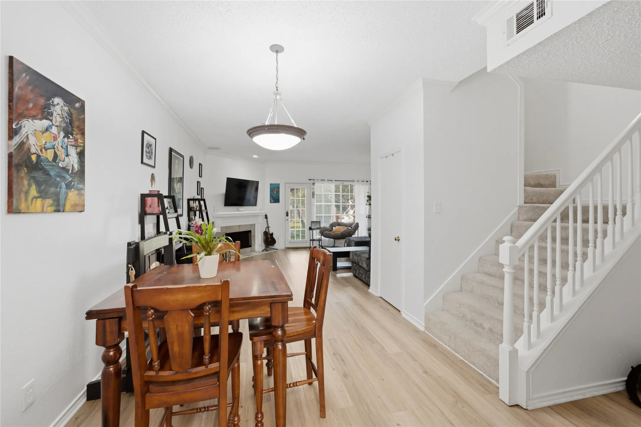 Open-concept living area featuring light wood-finish flooring, a contemporary fireplace, and a staircase with a white baluster railing