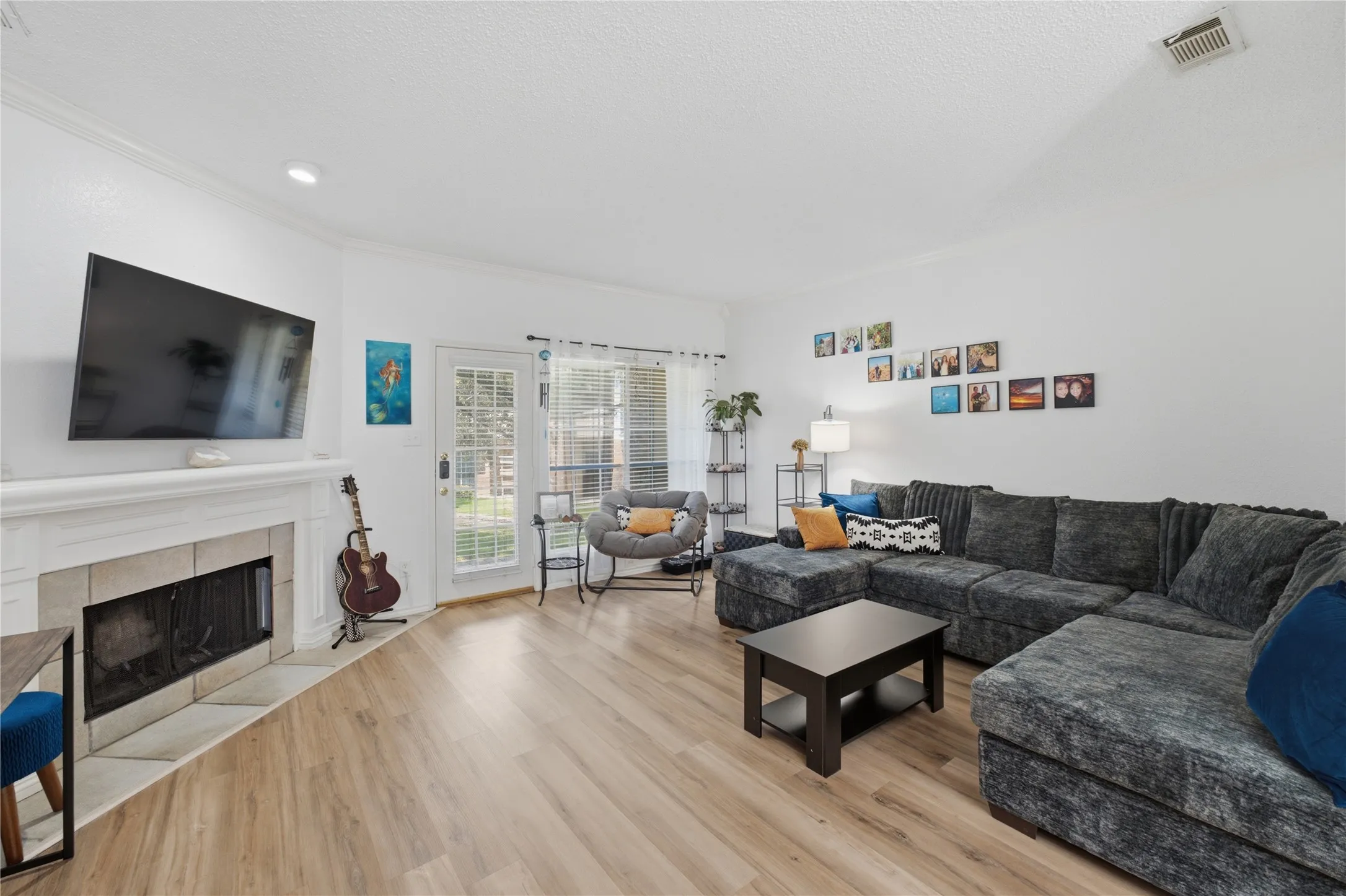 Spacious living area featuring light wood-finish flooring, a white-painted fireplace with a stone surround, and recessed lighting