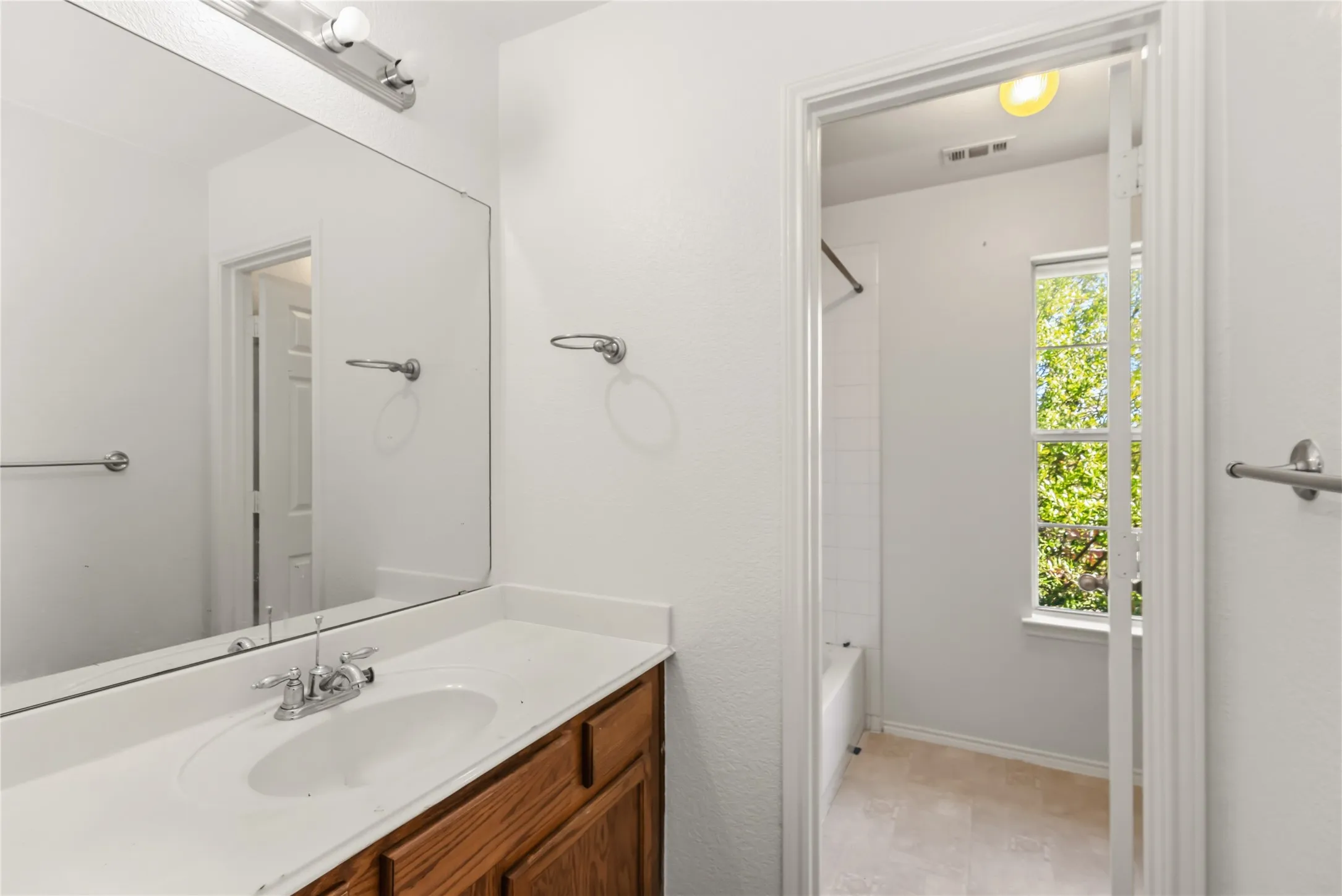 Bathroom featuring a wood-finish vanity with a white countertop and an integrated sink, a large wall mirror, and chrome fixtures