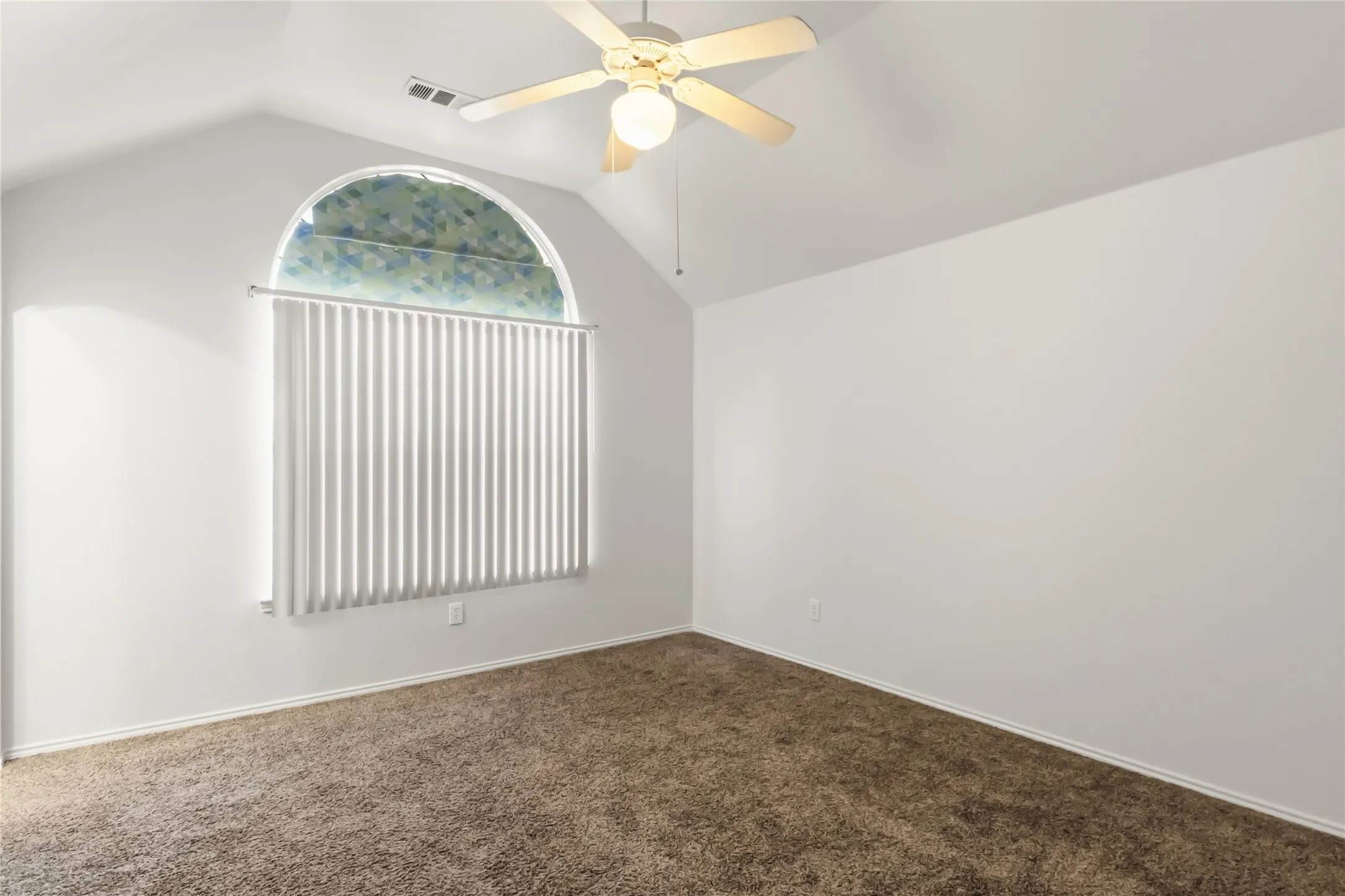 Vaulted ceiling with a ceiling fan, arched window with vertical blinds, and brown carpet flooring
