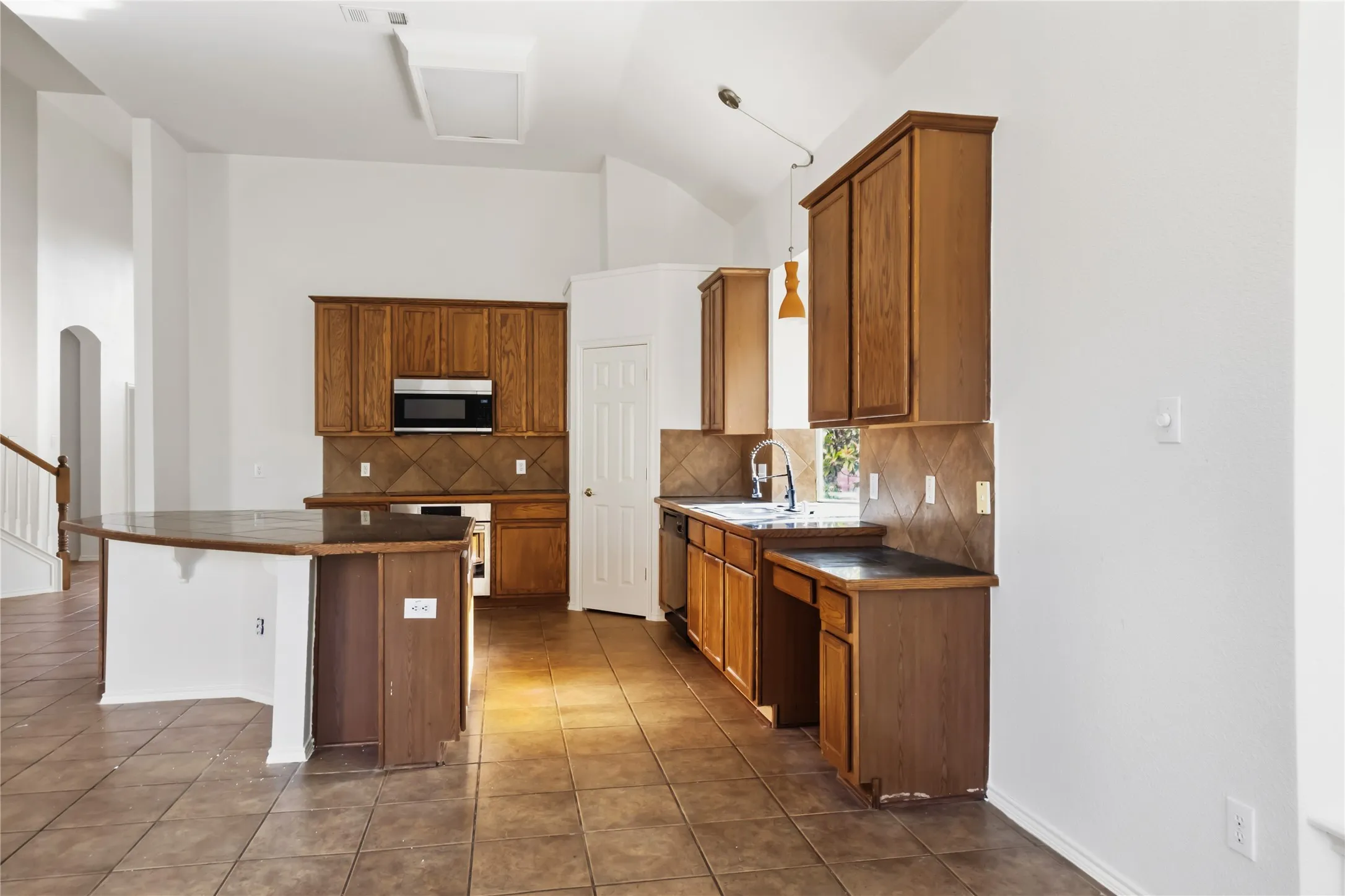 Kitchen featuring wood cabinetry, tile flooring, built-in microwave, and an island with countertop