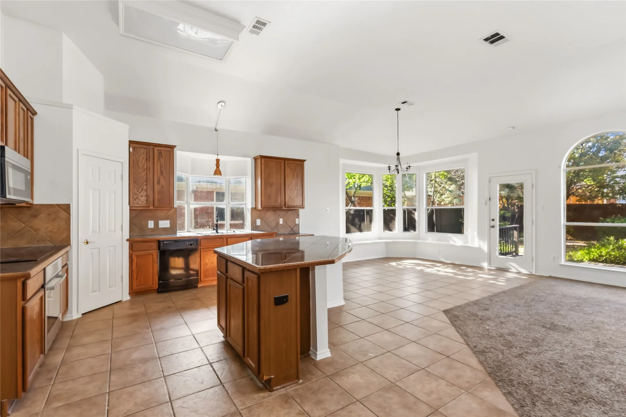 Kitchen featuring wood cabinetry, tile flooring, a kitchen island with a dark countertop, a bay window, and a vaulted ceiling