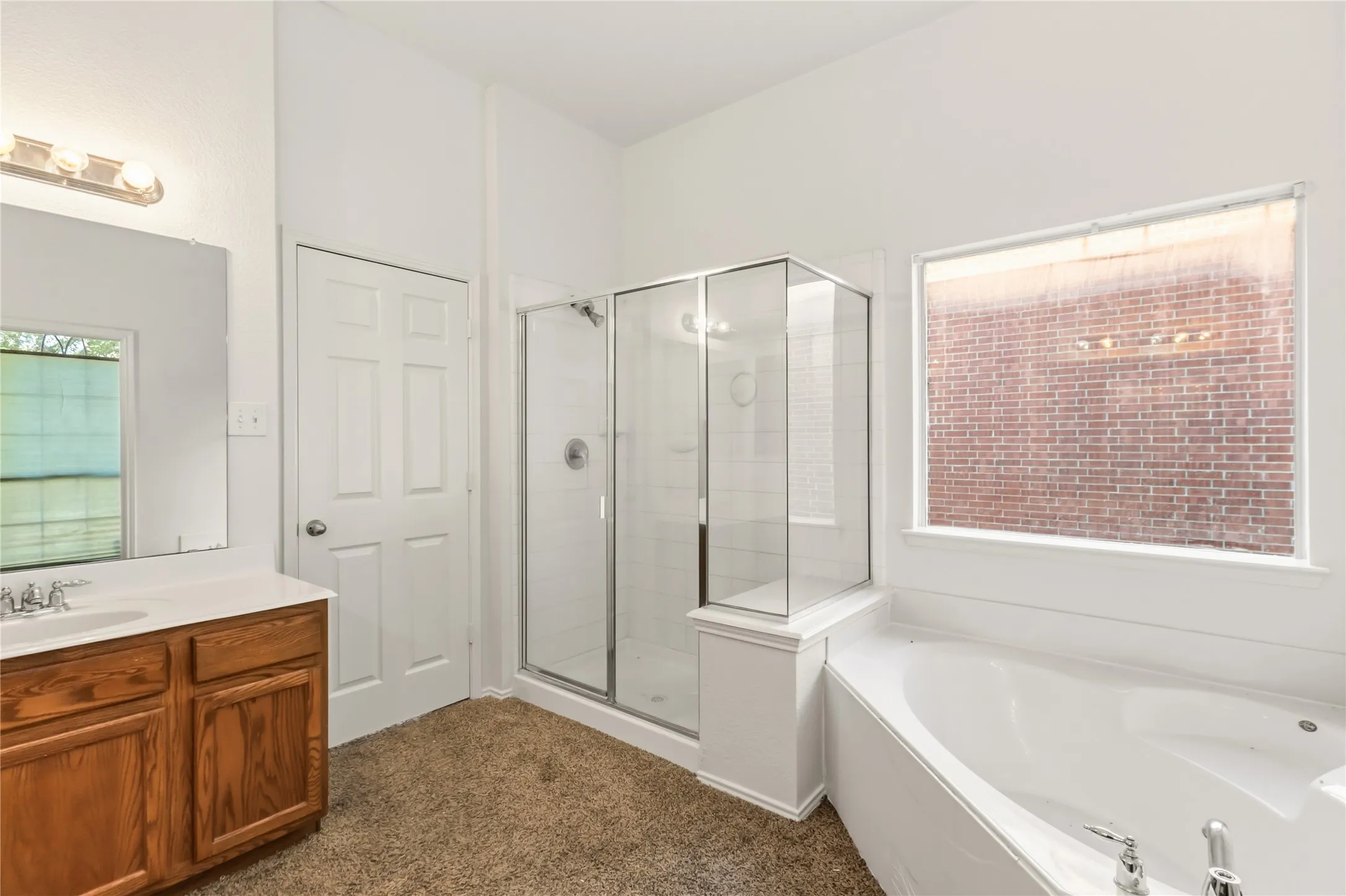 Spa-inspired primary bathroom featuring a freestanding soaking tub, corner walk-in shower enclosure with glass panels, dual-sink wood vanity with ample storage, ceramic tile flooring, and abundant natural light from a large window