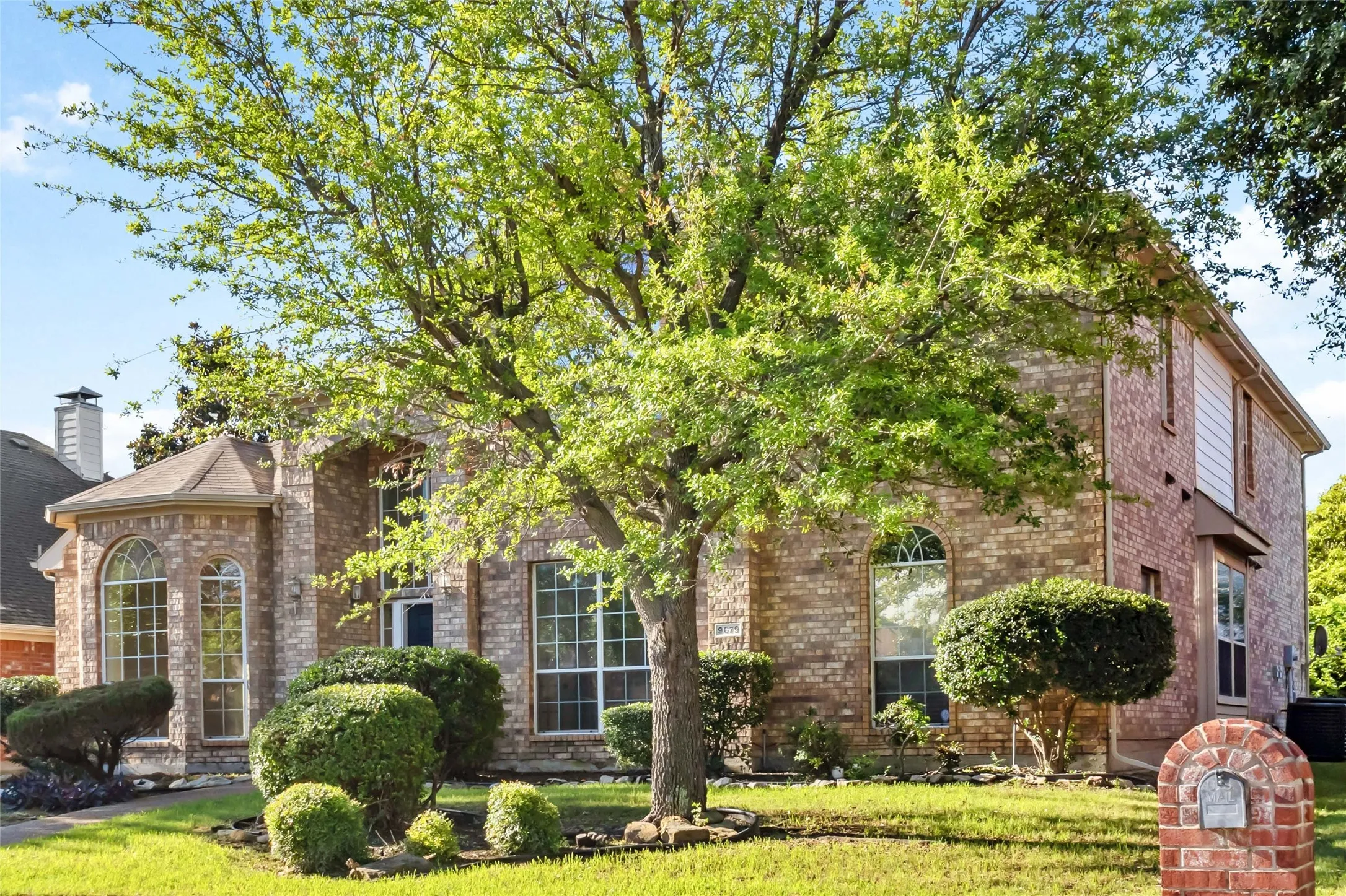 Brick facade with arched windows, mature landscaping, and a manicured lawn