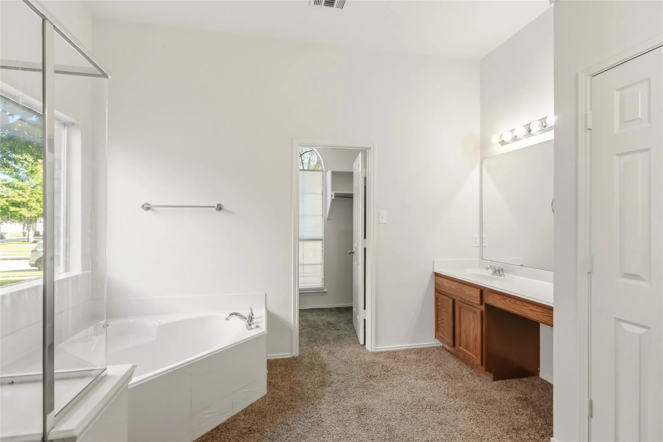 Vaulted ceiling, corner soaking tub, separate shower enclosure, wood-finish vanity with integrated sink, and wall-mounted mirror with vanity lighting