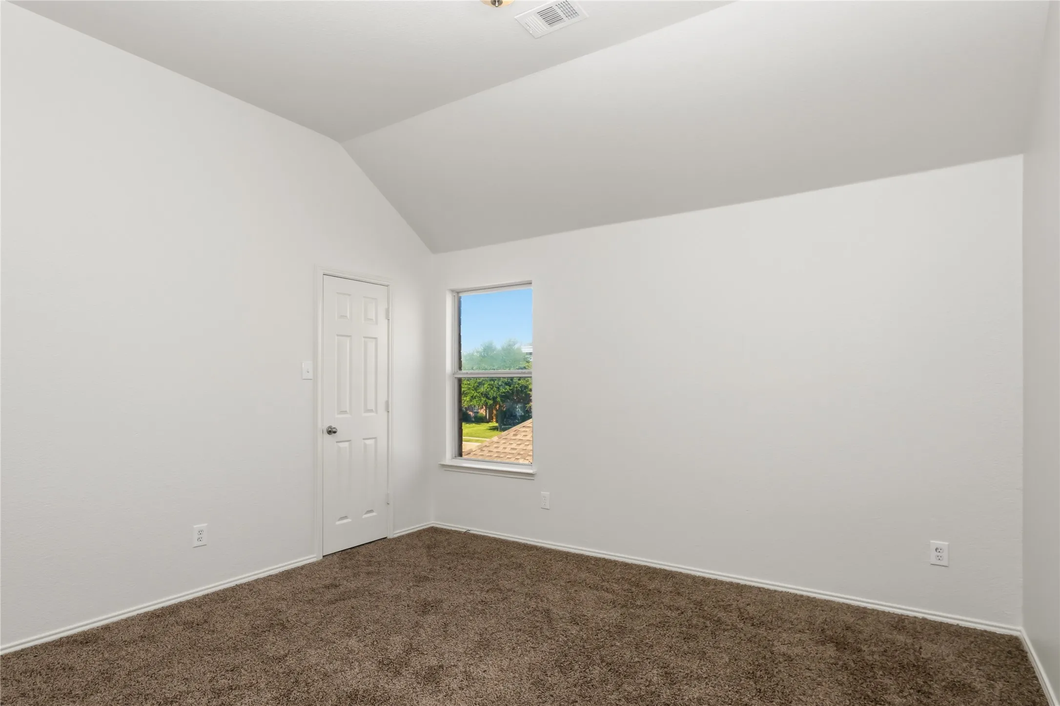 Vaulted ceiling with white walls, carpet flooring, and window with exterior visibility