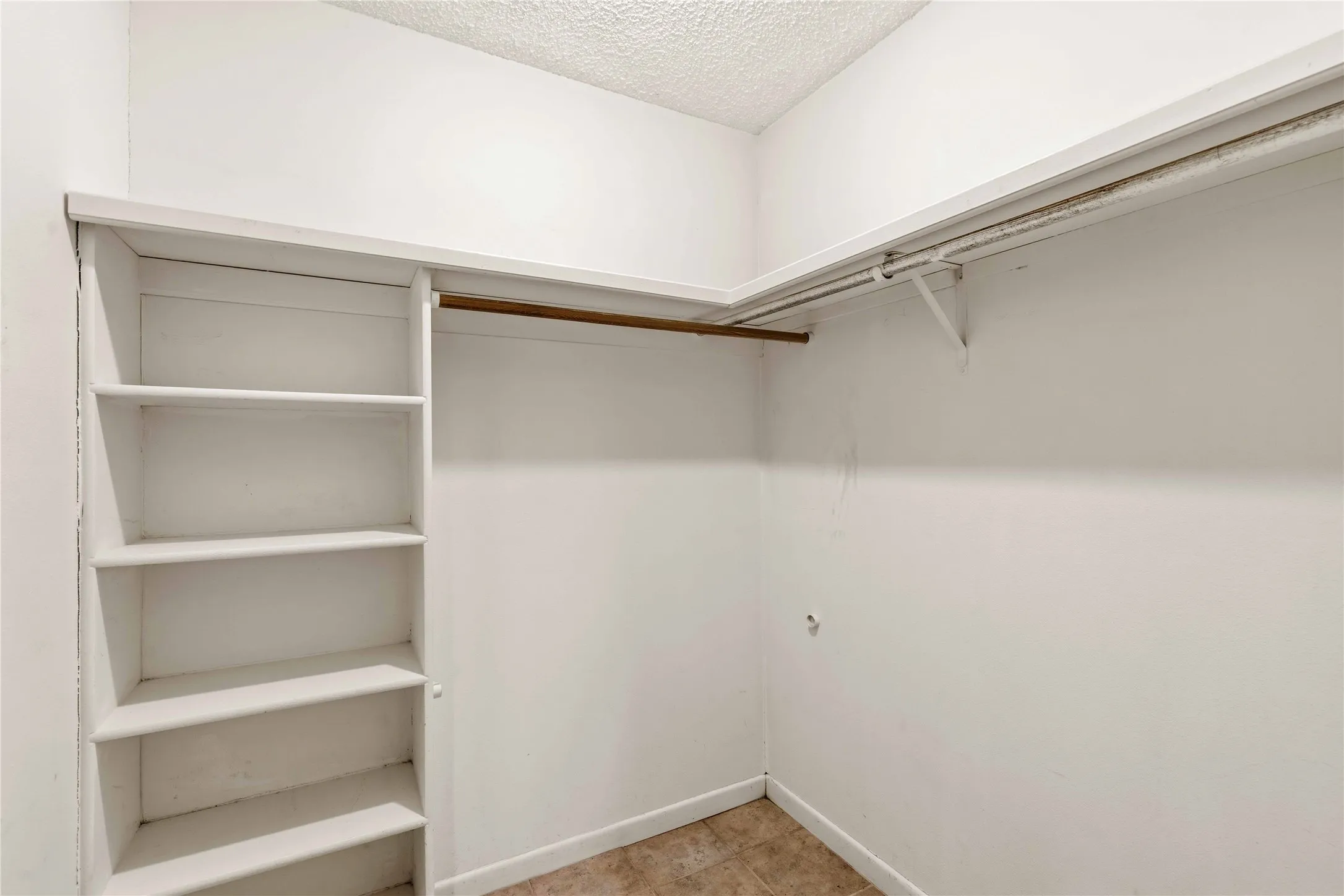 Built-in shelving and hanging rods offer versatile storage solutions within this closet space, featuring white walls and a textured ceiling