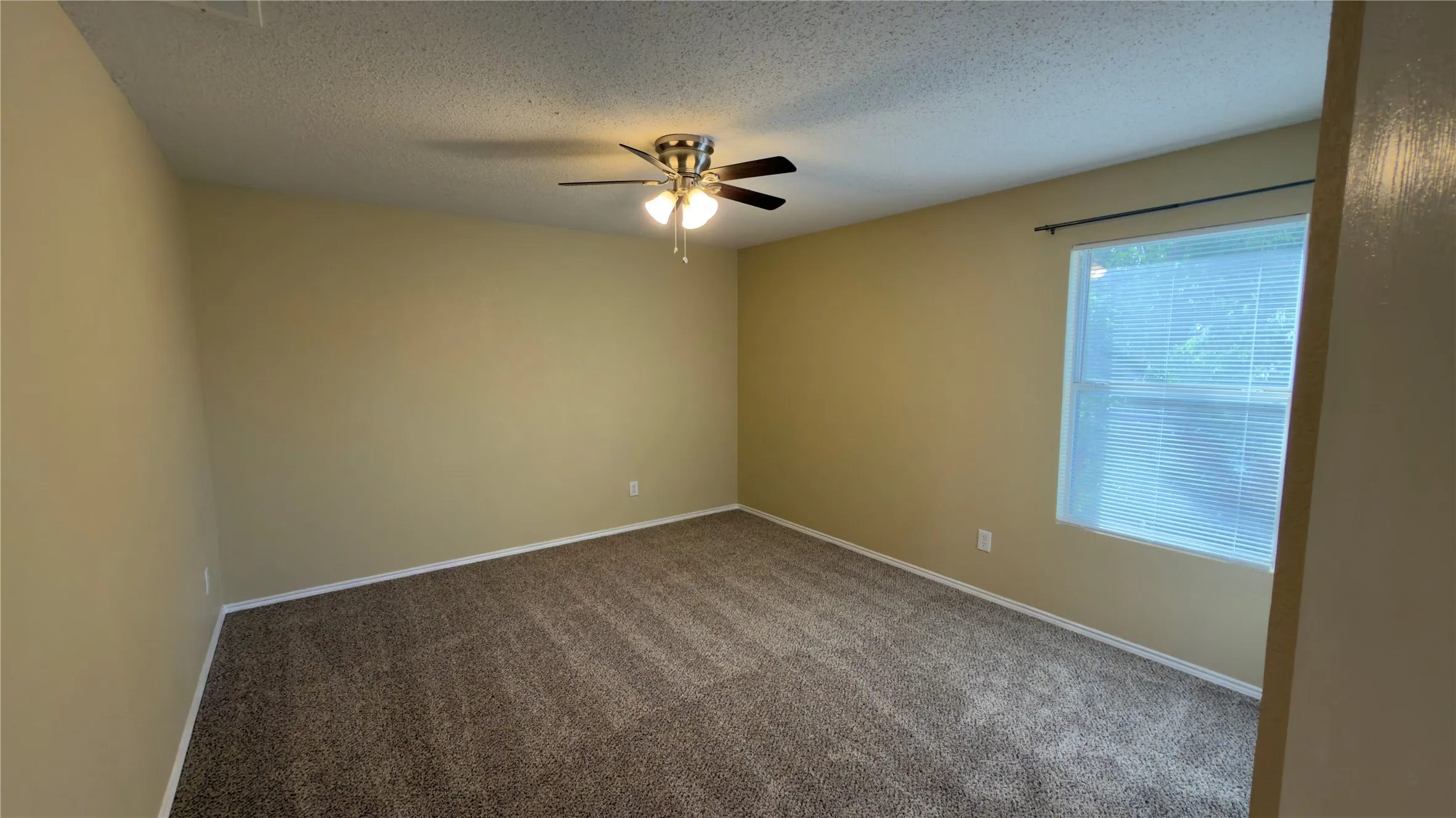 Spacious interior room featuring neutral-toned walls, textured ceiling, and carpeting