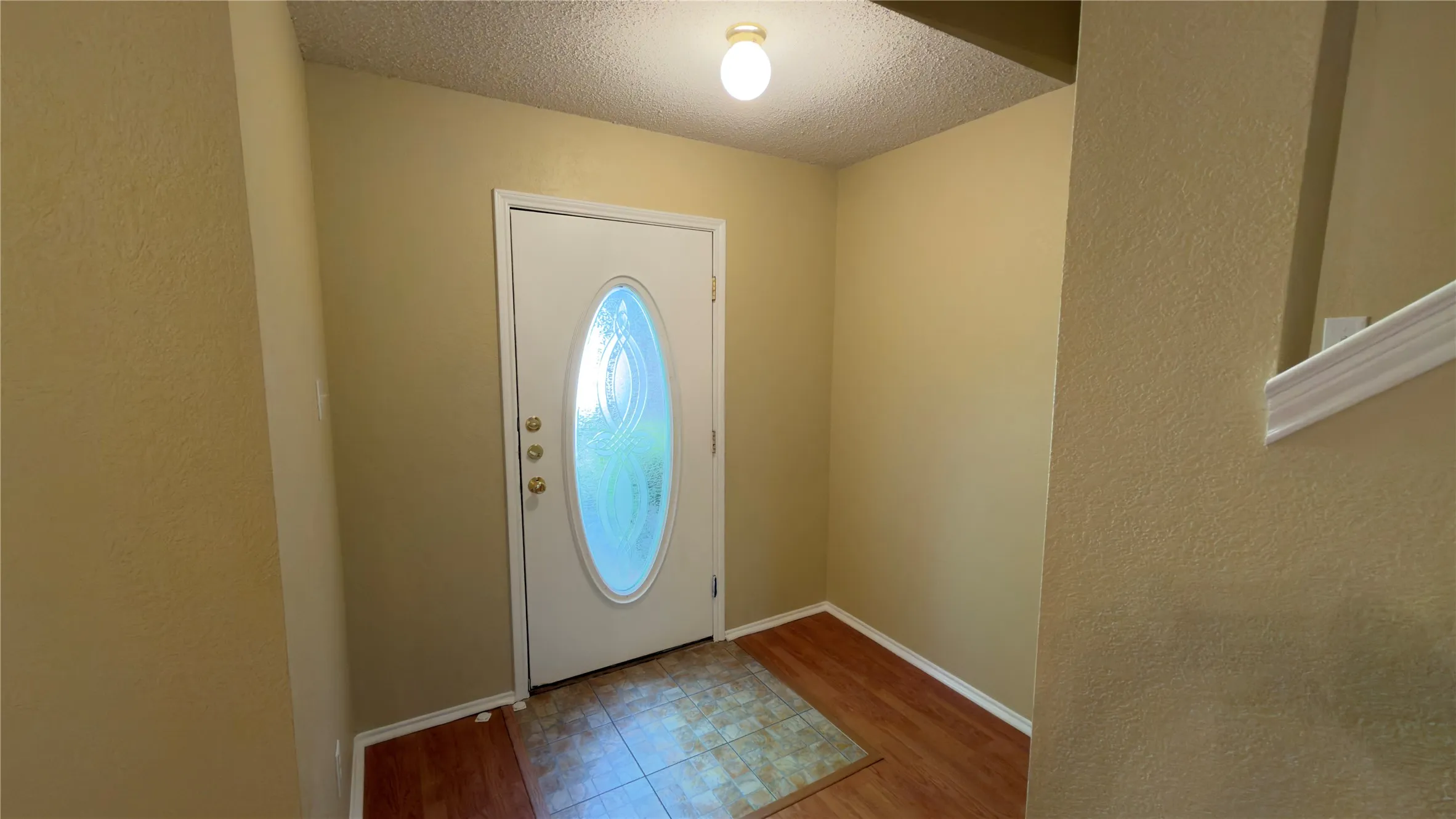 Entryway featuring a white door with an oval-shaped opaque glass insert, wood-finish flooring, and a flush-mount ceiling light fixture