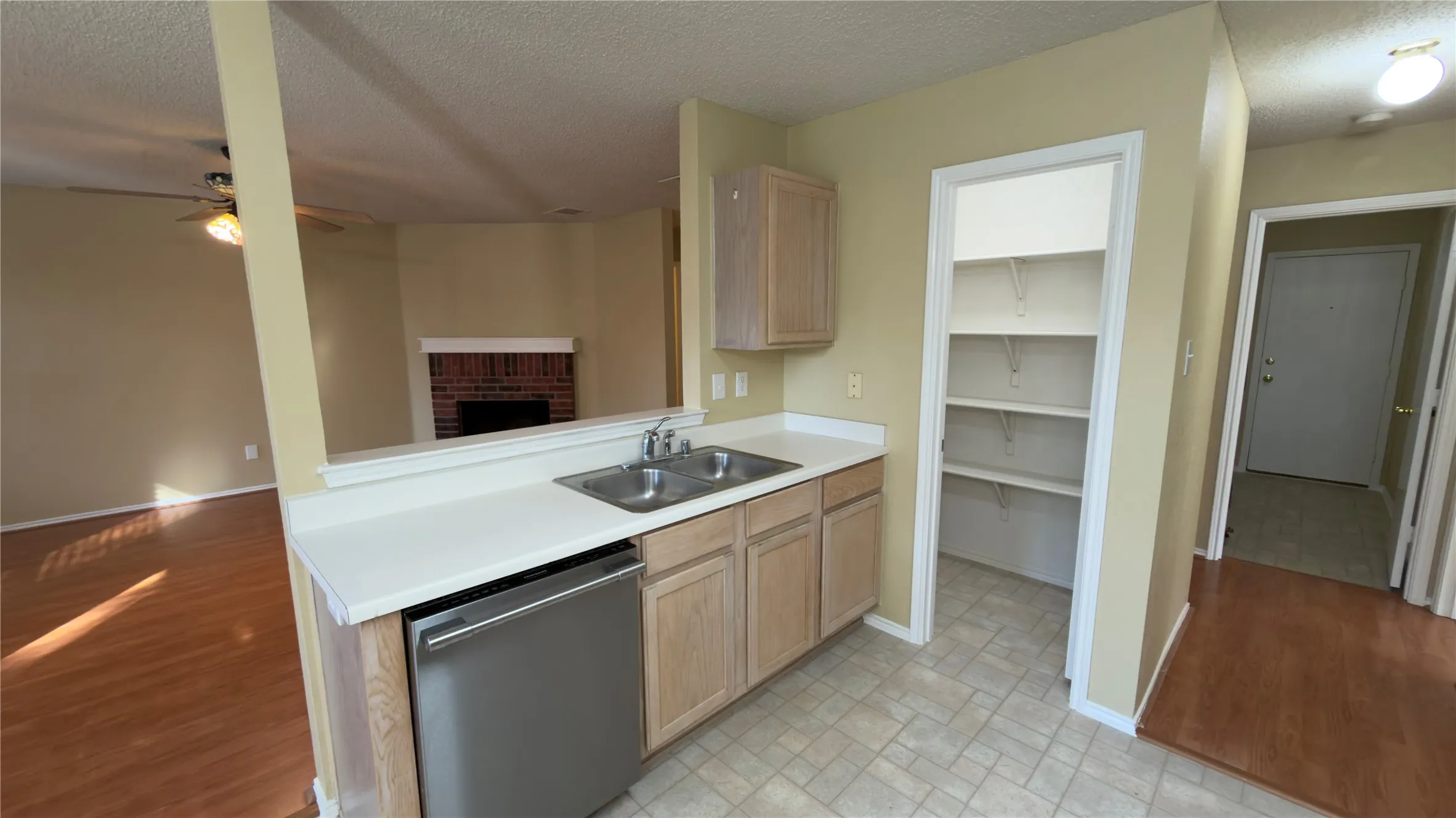 Kitchen featuring a stainless steel dishwasher, double basin sink, light wood-finish cabinetry, and white countertops