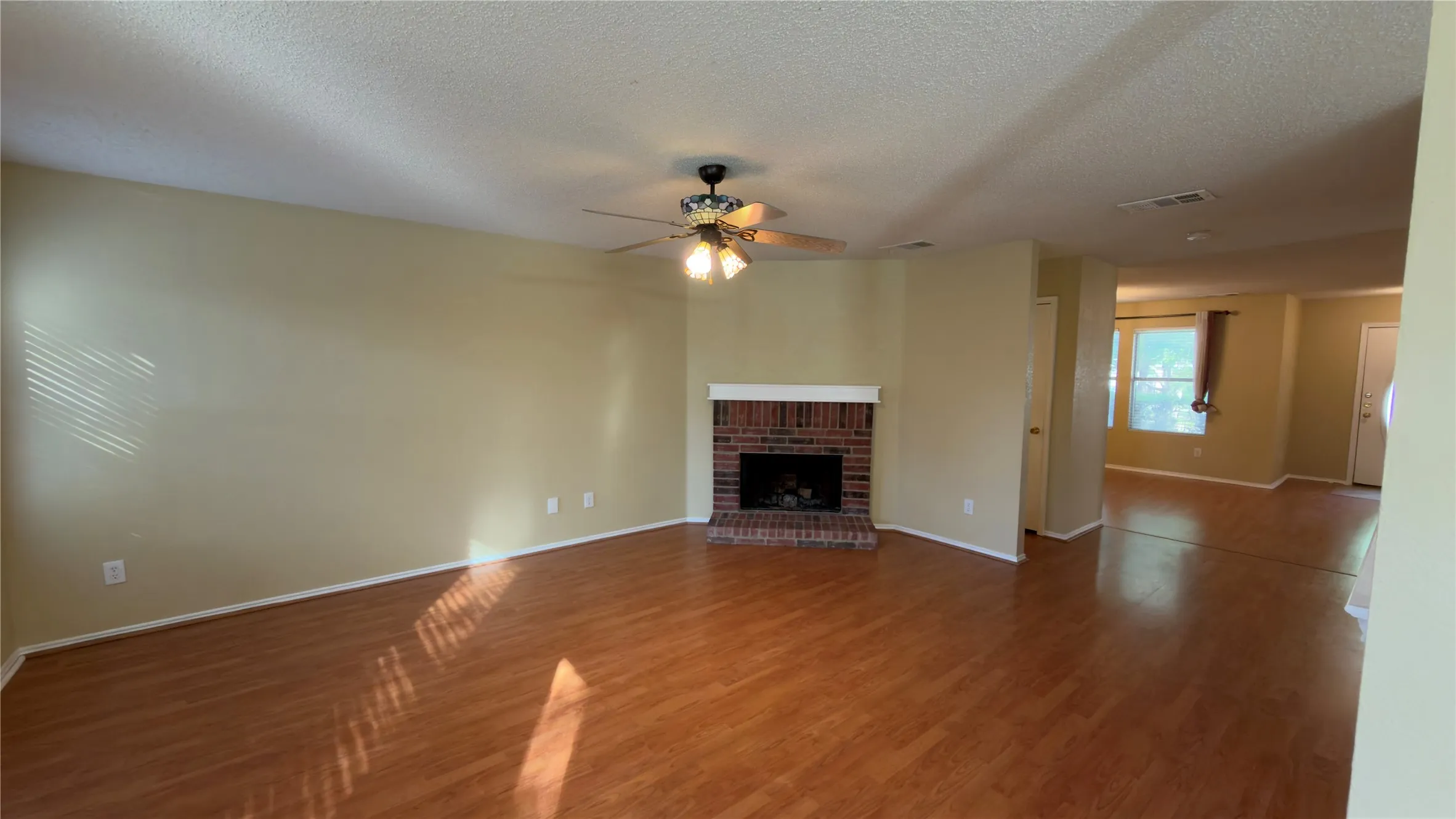 Spacious room featuring wood-finish flooring, a brick fireplace with a white mantel, and a ceiling fan with integrated lighting