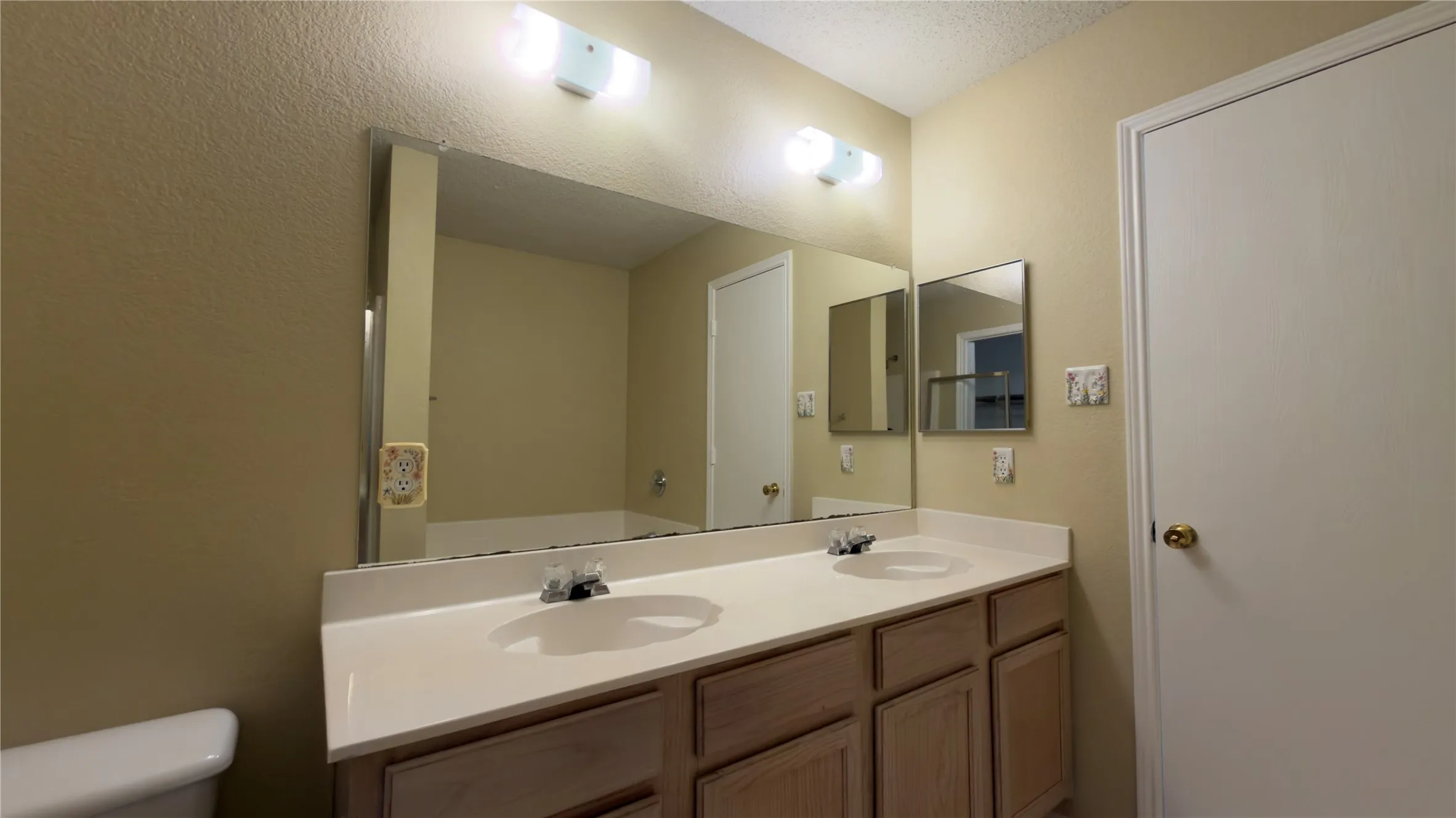 Bathroom vanity featuring dual sinks, a large wall-mounted mirror, wood-finish cabinetry, and overhead lighting