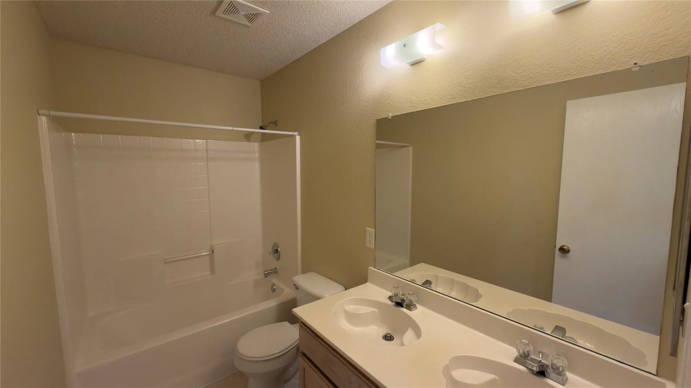 Bathroom featuring a dual-sink vanity with an integrated countertop, large wall-mounted mirror, and a combined tub and shower unit