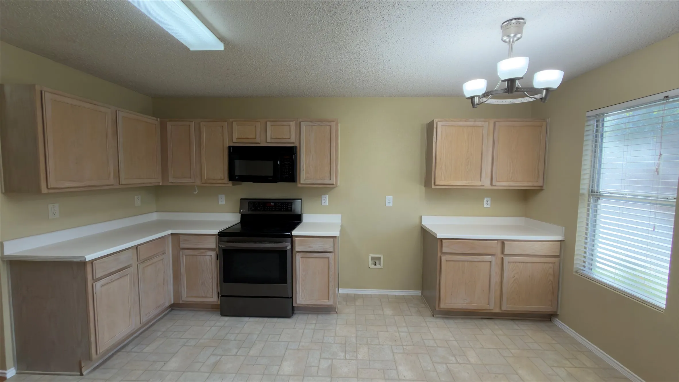 Kitchen featuring ample cabinetry with wood-finish doors, white countertops, and a black range with an overhead microwave