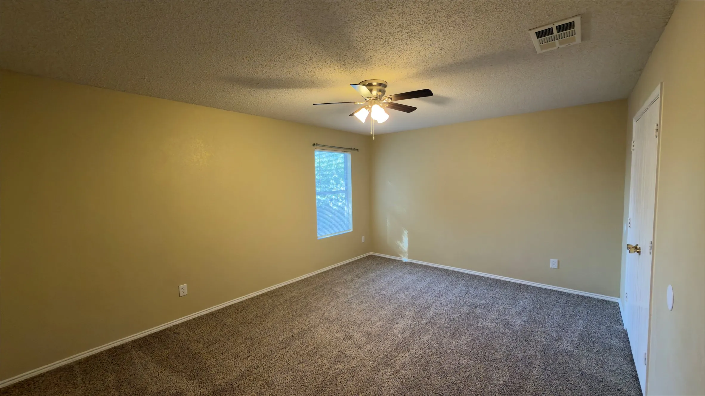 Carpeted room featuring a ceiling fan with light fixture, a single window, and a white interior door with a brass-toned knob