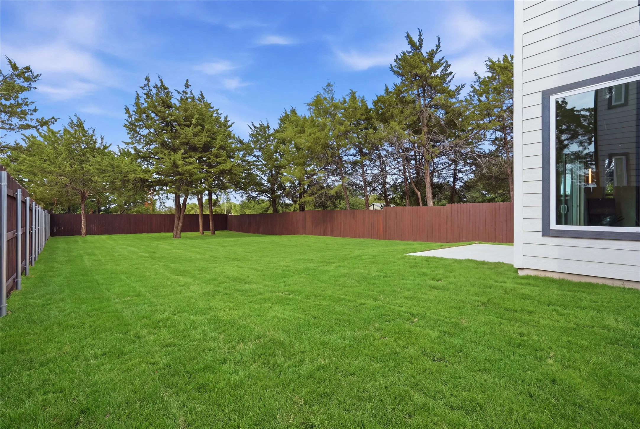 Expansive green lawn with a privacy fence, mature trees, and a concrete patio