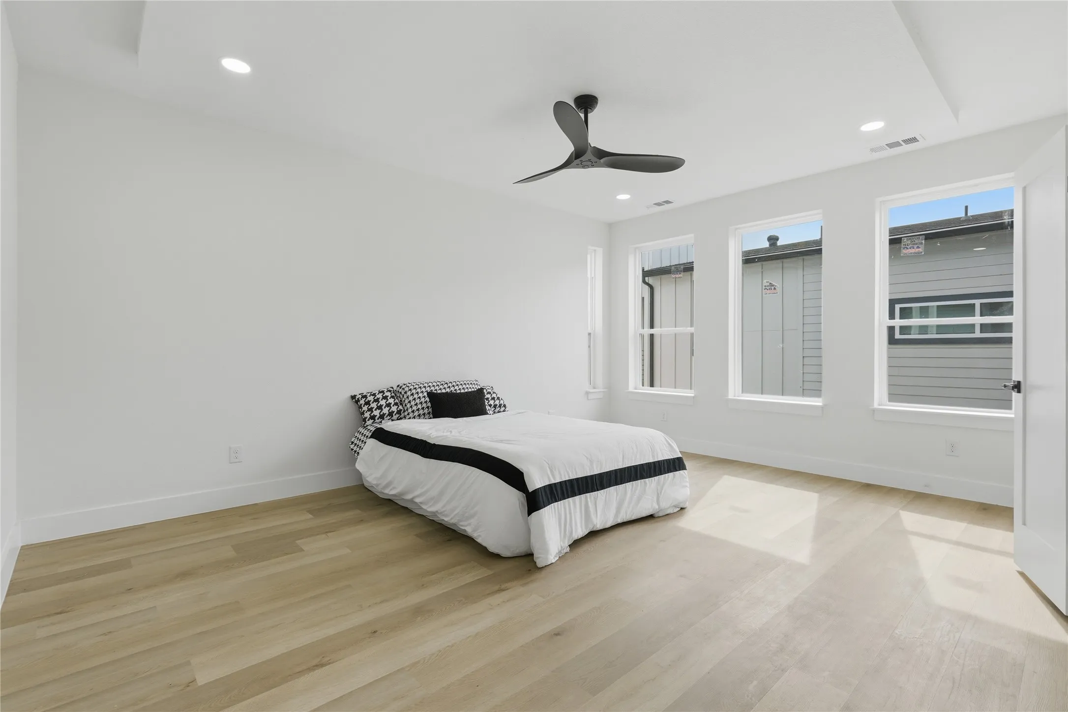 Recessed lighting, wood-finish flooring, contemporary ceiling fan, multiple windows, and a tray ceiling