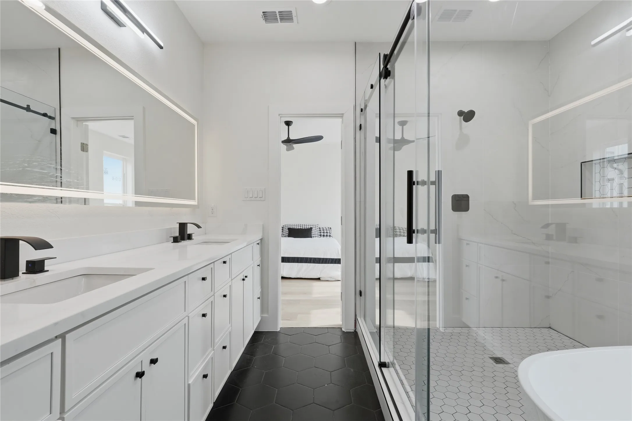 Dual vanity with integrated sinks, back-lit mirrors, matte black fixtures, frameless glass shower enclosure, and hexagon tile flooring