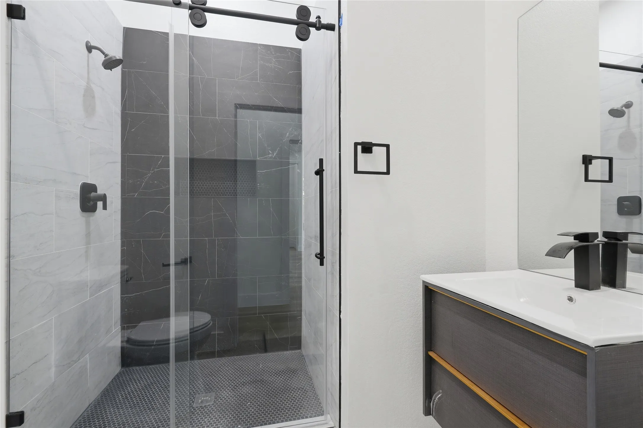 Glass-enclosed shower with matte black fixtures and a sliding barn door