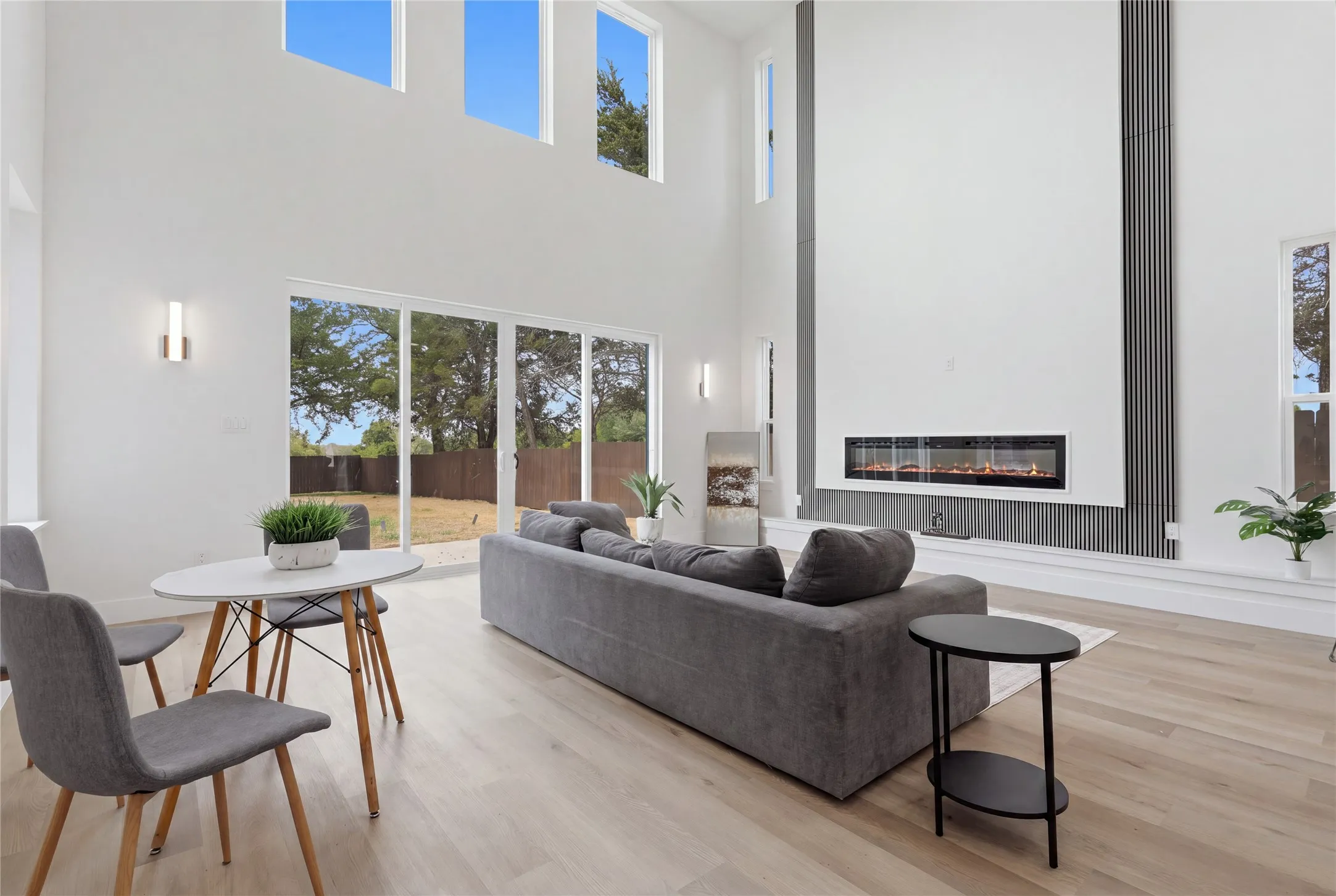 Soaring ceilings with transom windows, wood-finish flooring, a linear electric fireplace, and a wall of glass sliding doors