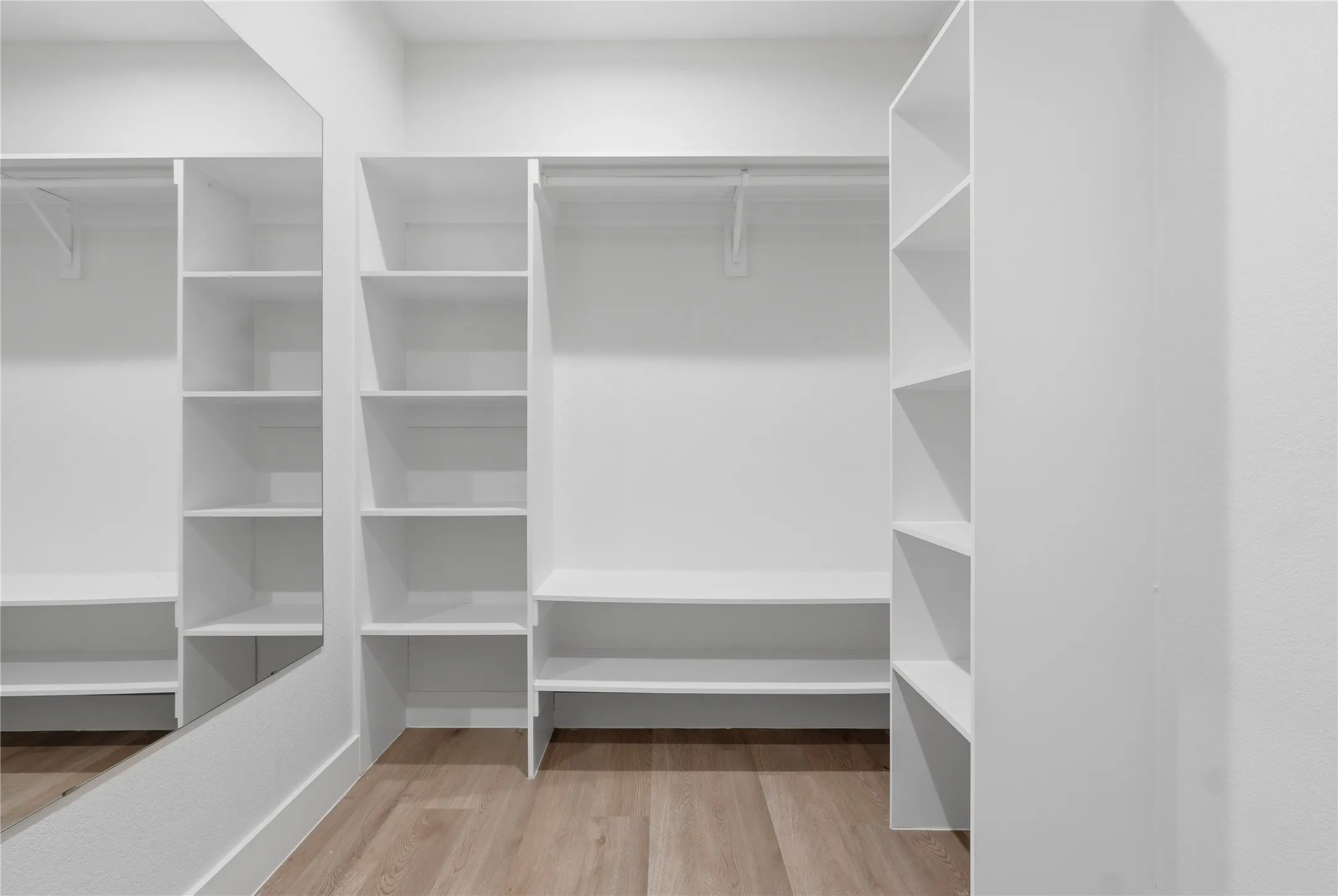 Custom closet system with white shelving, hanging rods, and integrated full-length mirror