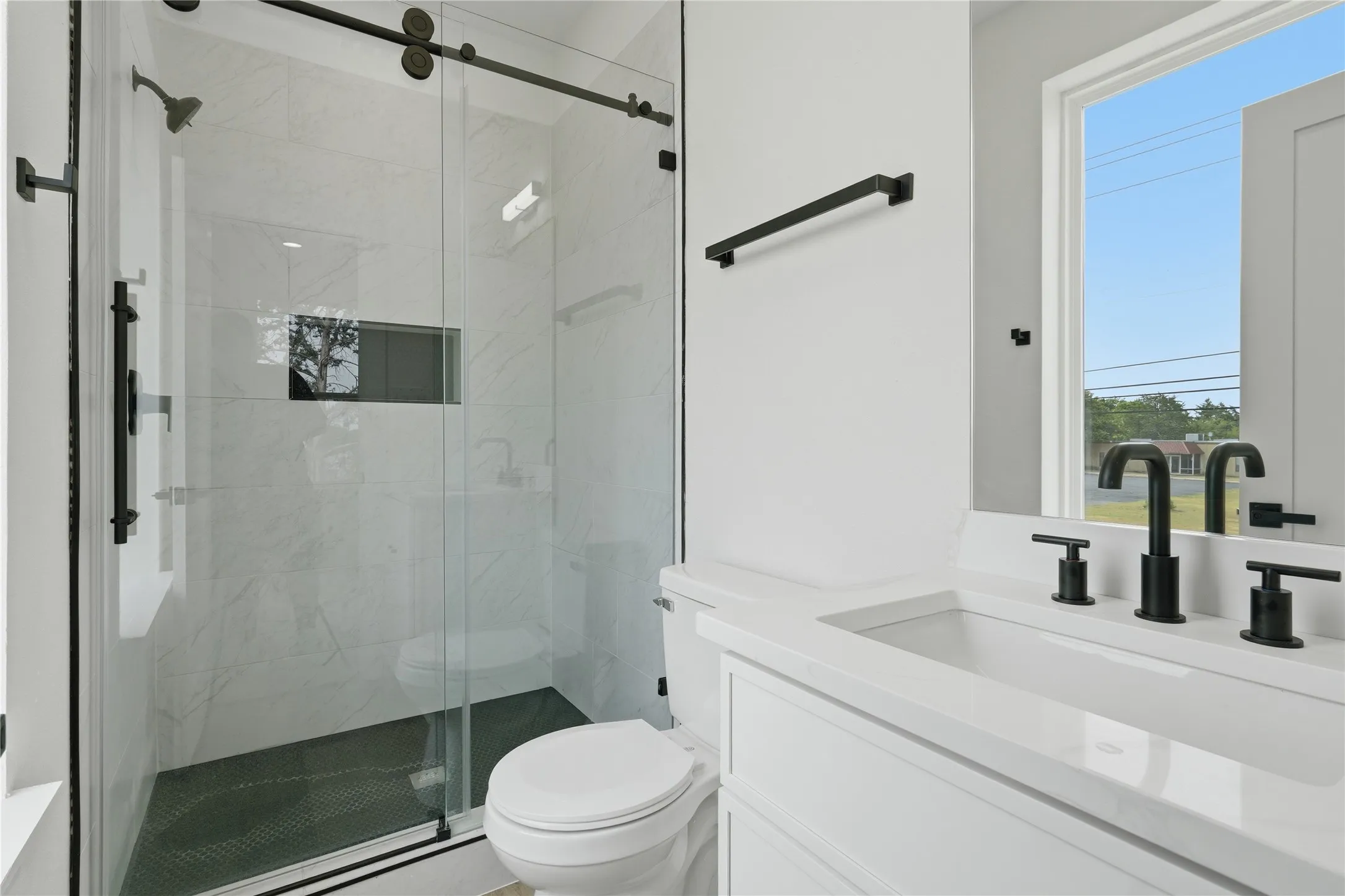 Glass-enclosed shower with a matte black barn door style frame, tiled shower walls, and a built-in shower niche
