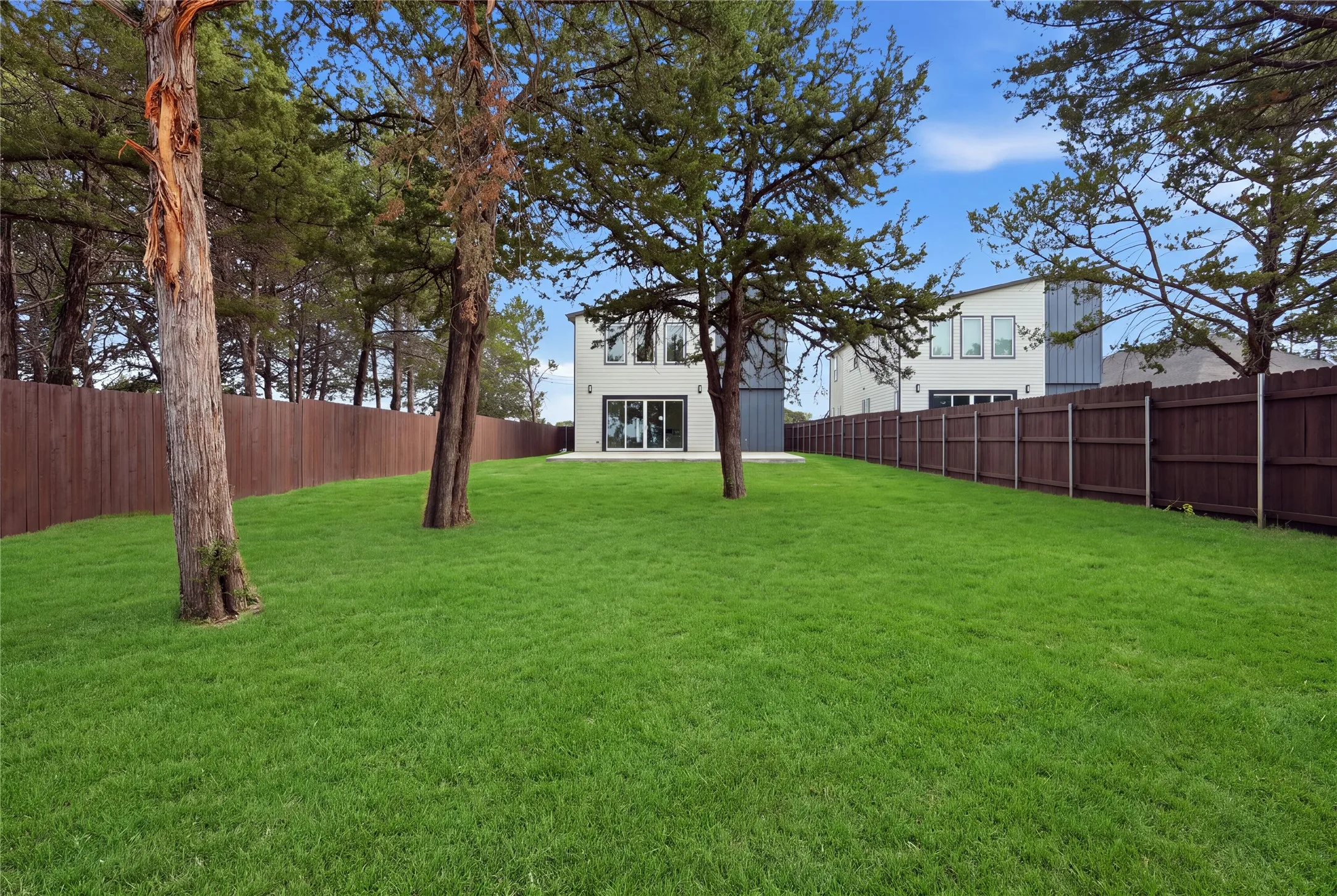 Expansive green lawn with mature trees and a private wood fence