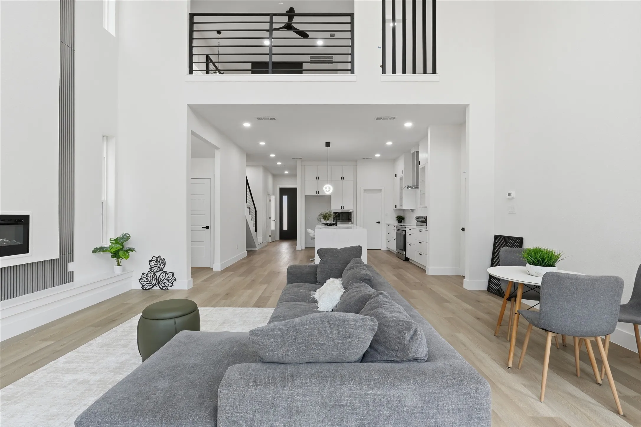 Two-story living area featuring wood-finish flooring, a contemporary fireplace, recessed lighting, and a kitchen with white cabinetry