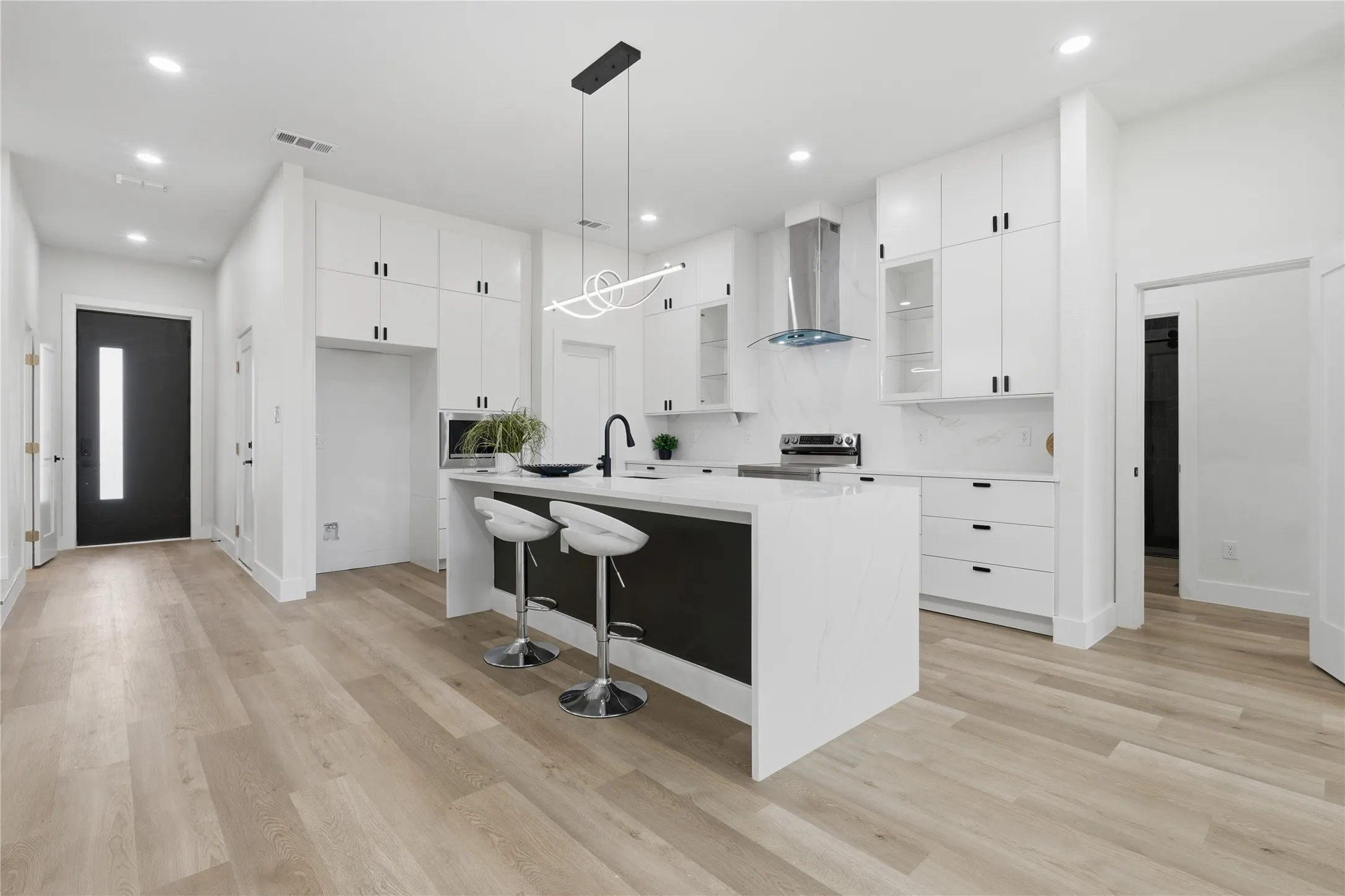 Open-concept kitchen with a central island, white cabinetry, integrated appliances, and wood-finish flooring